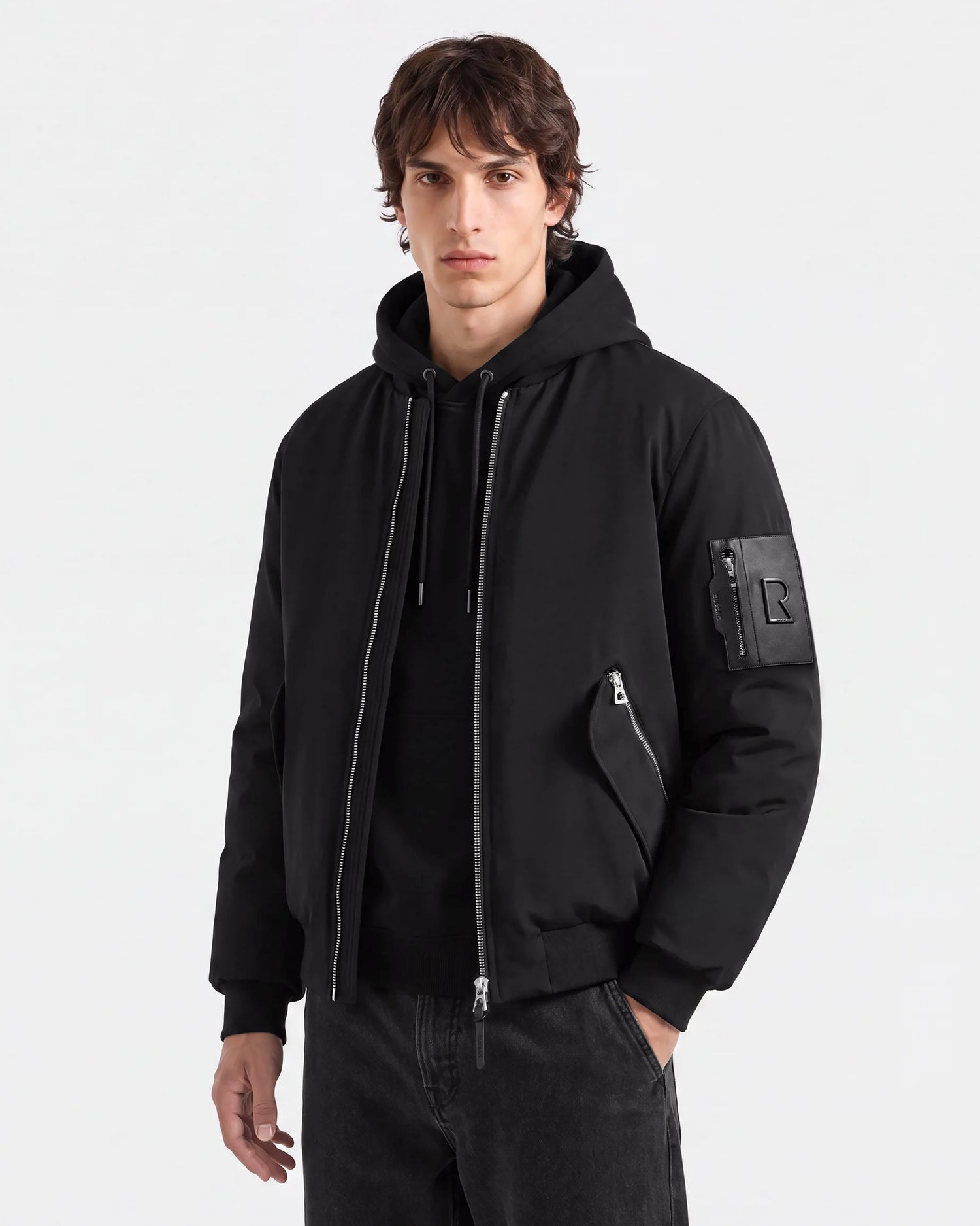 A person wearing the Rudsak DYLAN - 6125593 Black men's aviator bomber jacket—with zippered pockets, a faux fur collar, and paired with black pants—stands against a plain light background, facing forward with a neutral expression.