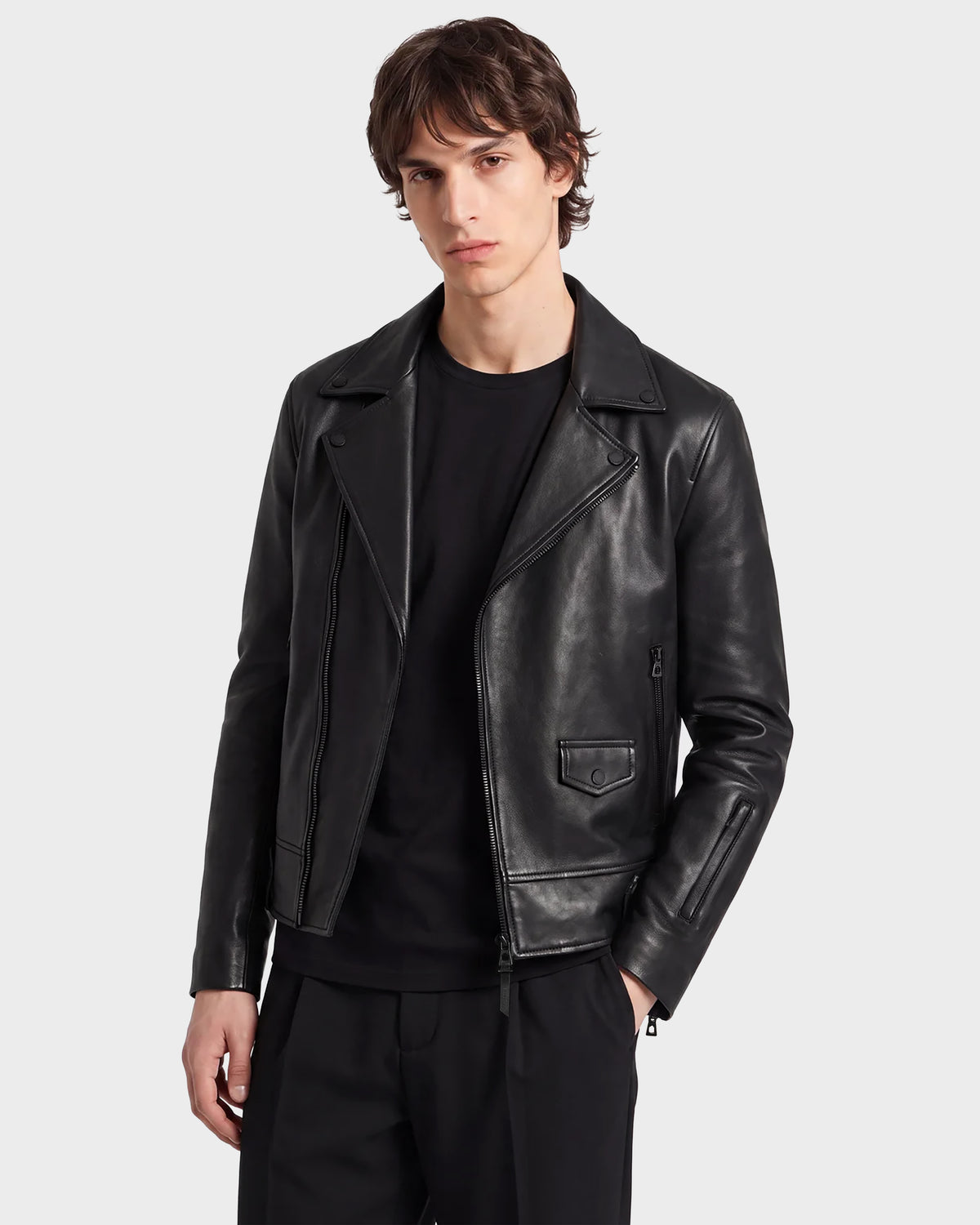 A person with medium-length brown hair wears the RUDSAK DAREG - 6122004 BLACK lamb leather biker jacket—an undeniable wardrobe essential—over a black shirt and black pants, standing against a plain light background.