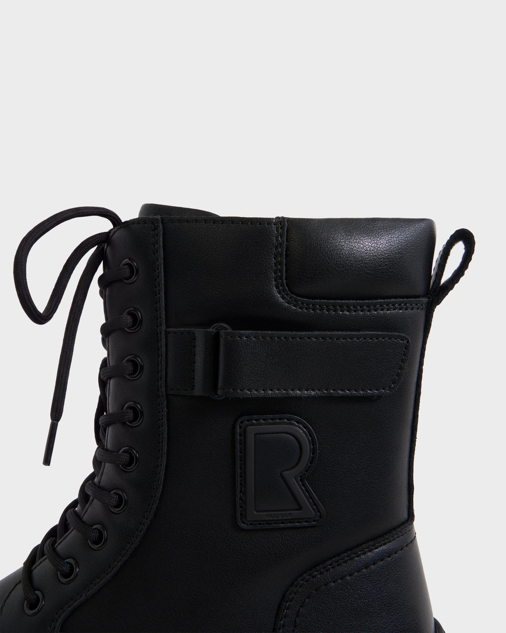 DEREK - 6226506 Black by Rudsak: black combat-style boot with laces, side Velcro strap, and embossed R logo. Shown from the side on a plain white background.