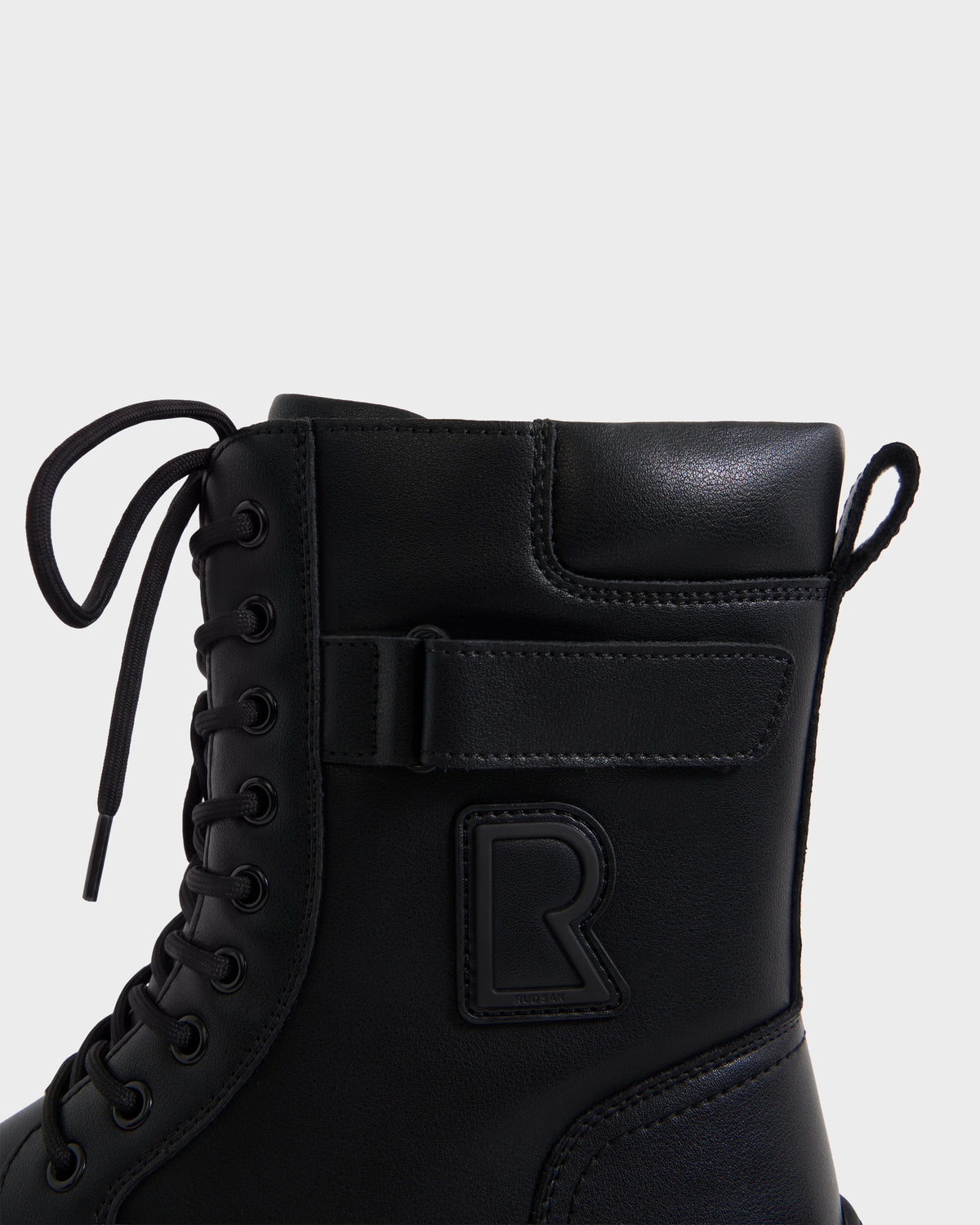 DEREK - 6226506 Black by Rudsak: black combat-style boot with laces, side Velcro strap, and embossed R logo. Shown from the side on a plain white background.
