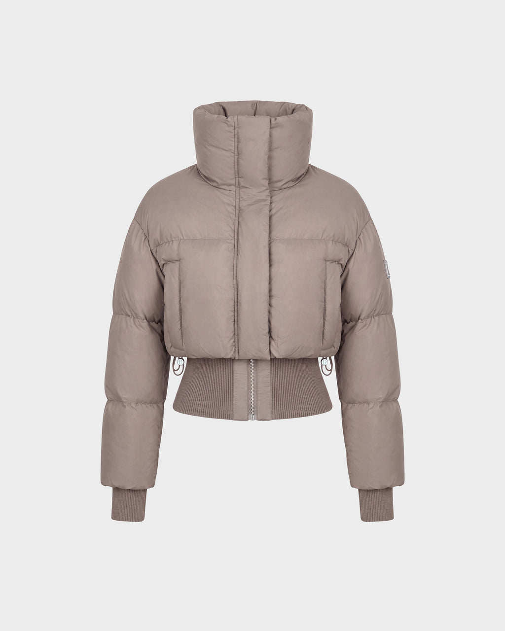 The Rudsak DONYA - 8126516 Cement is a taupe-colored, cropped women’s down puffer jacket made with RDS-certified down, featuring a high collar along with ribbed cuffs and hem, shown against a plain white background.