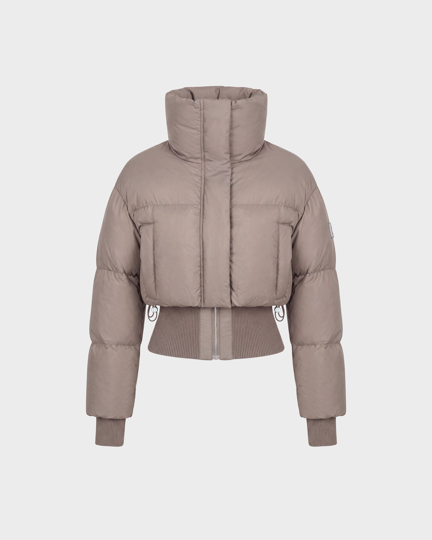 The Rudsak DONYA - 8126516 Cement is a taupe-colored, cropped women’s down puffer jacket made with RDS-certified down, featuring a high collar along with ribbed cuffs and hem, shown against a plain white background.