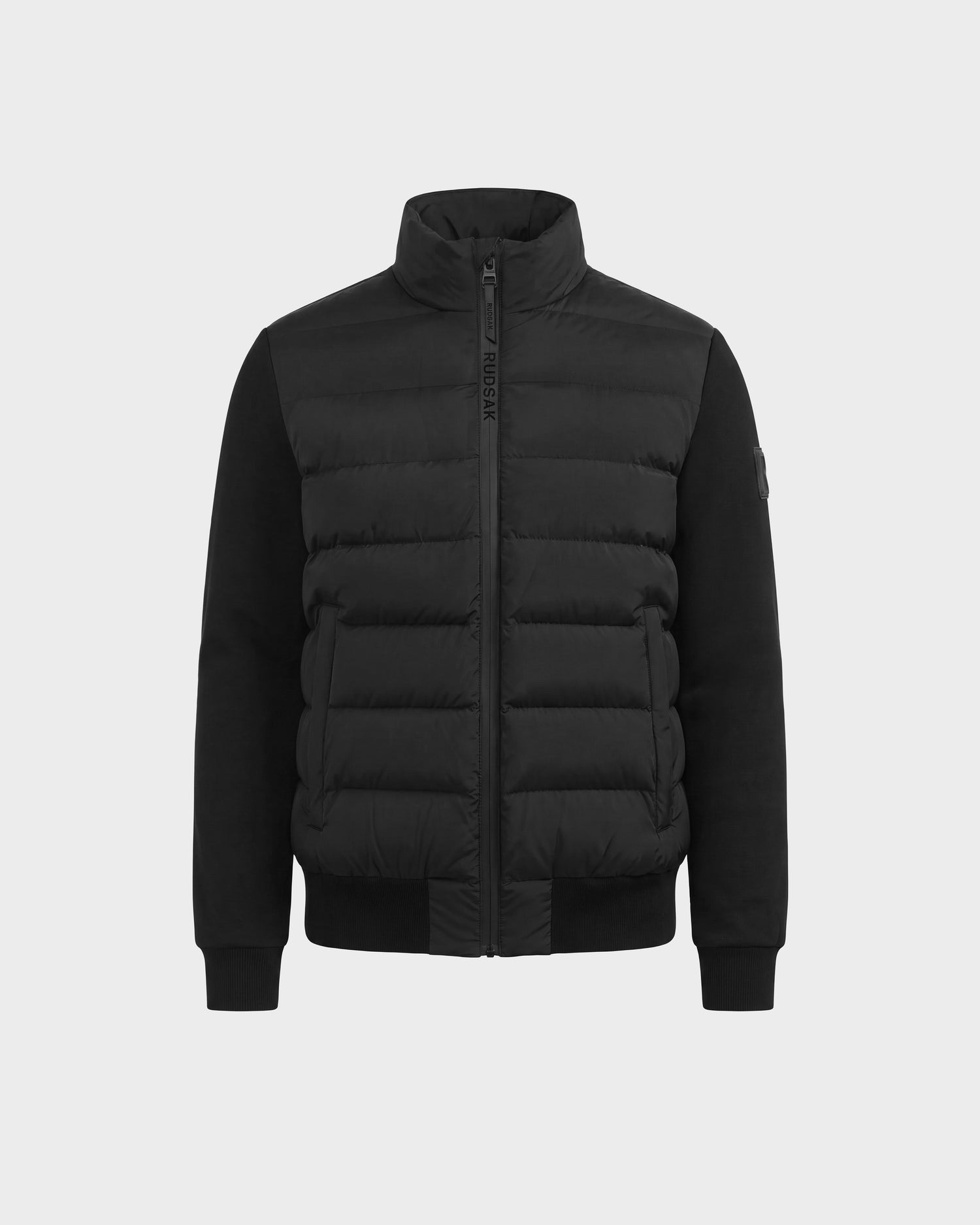 The EUGENE - 6124721 Black men's hybrid jacket by Rudsak features quilted padded sections on the front, smooth performance luxury fabric sleeves, a high collar, zip closure, and ribbed cuffs. This black puffer jacket is displayed against a plain light background.