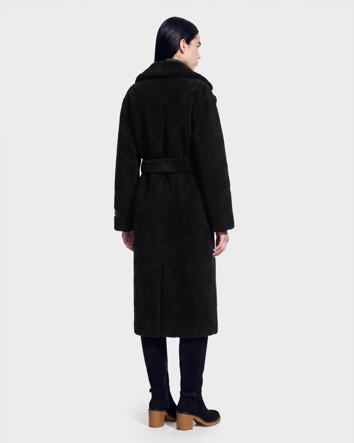 A person with long dark hair is seen from behind, wearing the Rudsak FRANCIE - 8126873 Black belted coat and black boots, set against a plain light background. This striking look is now available for pre-order and is expected to ship by September 15th.