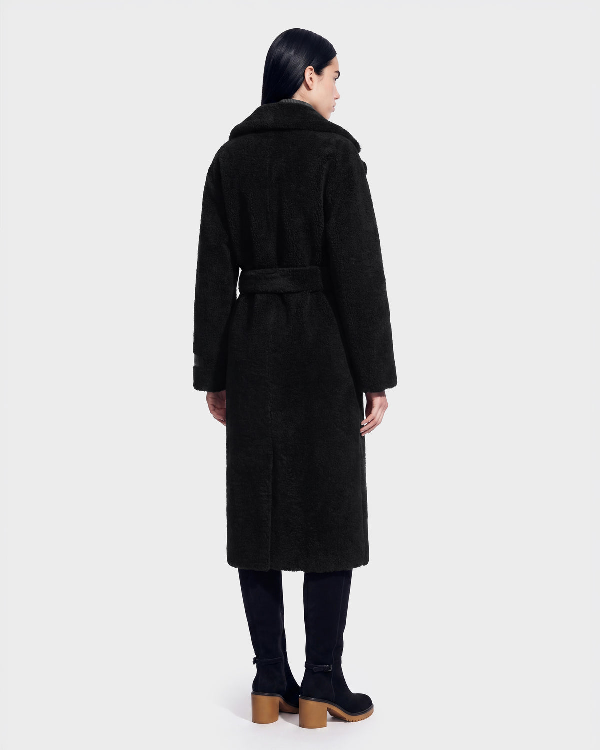 A person with long dark hair is seen from behind, wearing the Rudsak FRANCIE - 8126873 Black belted coat and black boots, set against a plain light background. This striking look is now available for pre-order and is expected to ship by September 15th.