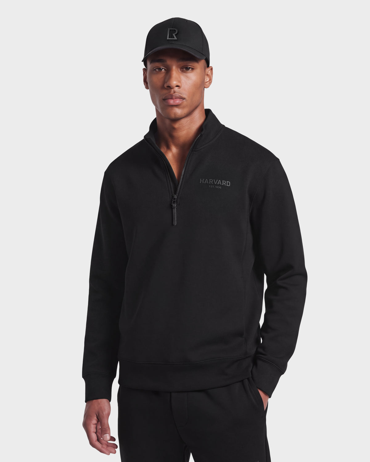 A man wearing the Rudsak FREMONT HV - H525501 Black pullover sweatshirt and a black baseball cap stands facing forward with a neutral expression against a plain white background.