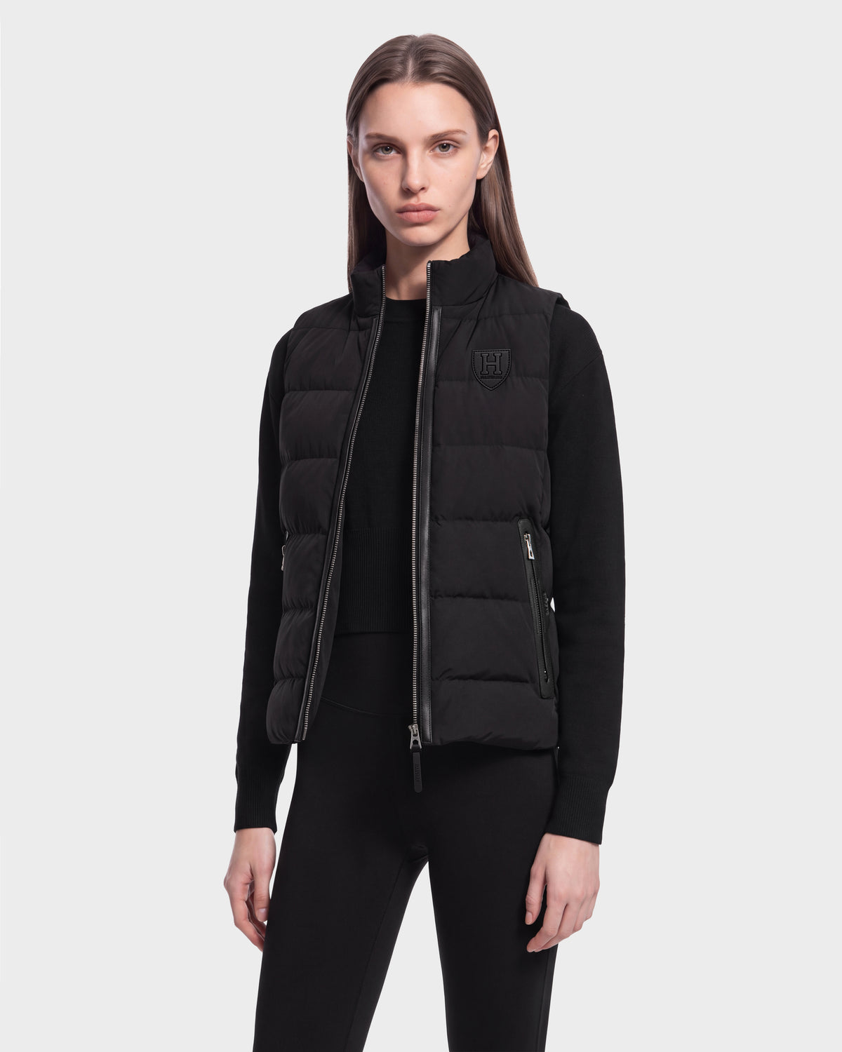 A person wearing the Rudsak GABRIELA HV - H125507 Black puffer vest over a black long-sleeve top and black pants stands facing forward against a plain light background.