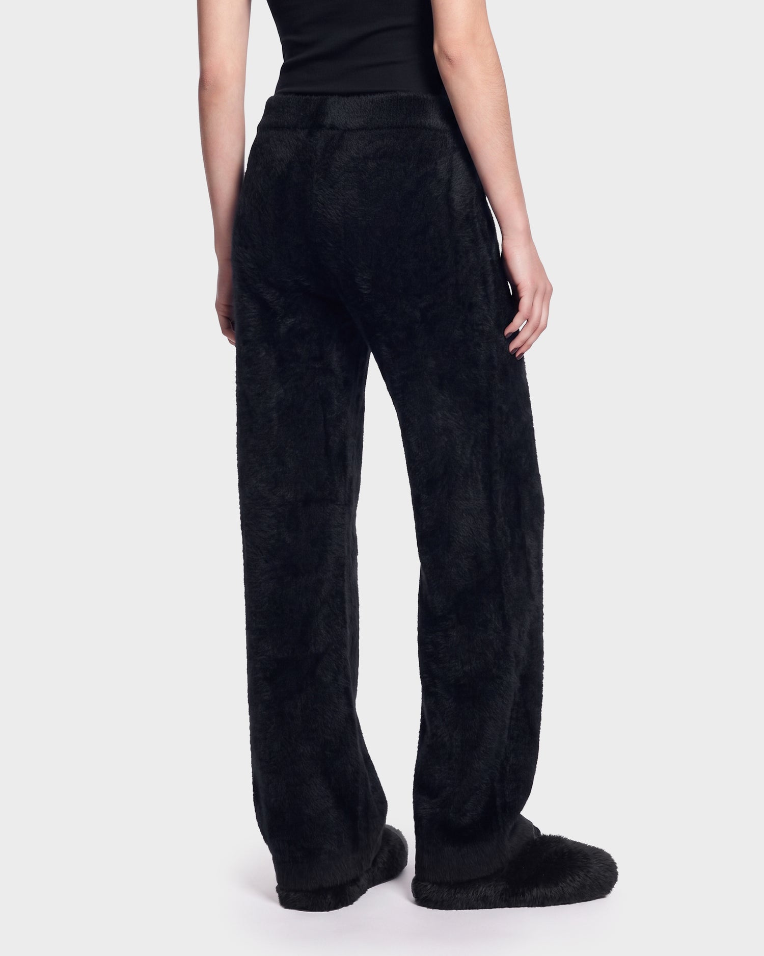 A person wearing the Rudsak GENESIS - 8526506 Black fuzzy pants and matching slippers stands with their back to the camera against a plain light background.