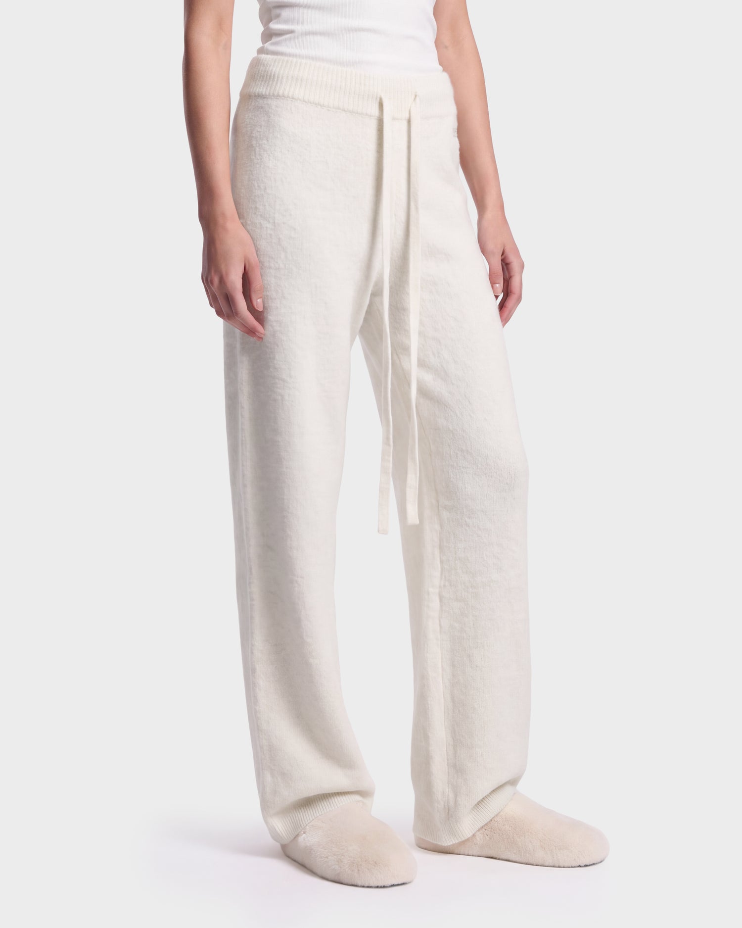 A person is shown from the midsection down, wearing Rudsak’s GENESIS - 8526506 Iceland cream-colored loose knit drawstring pants with matching slippers, set against a plain light background.