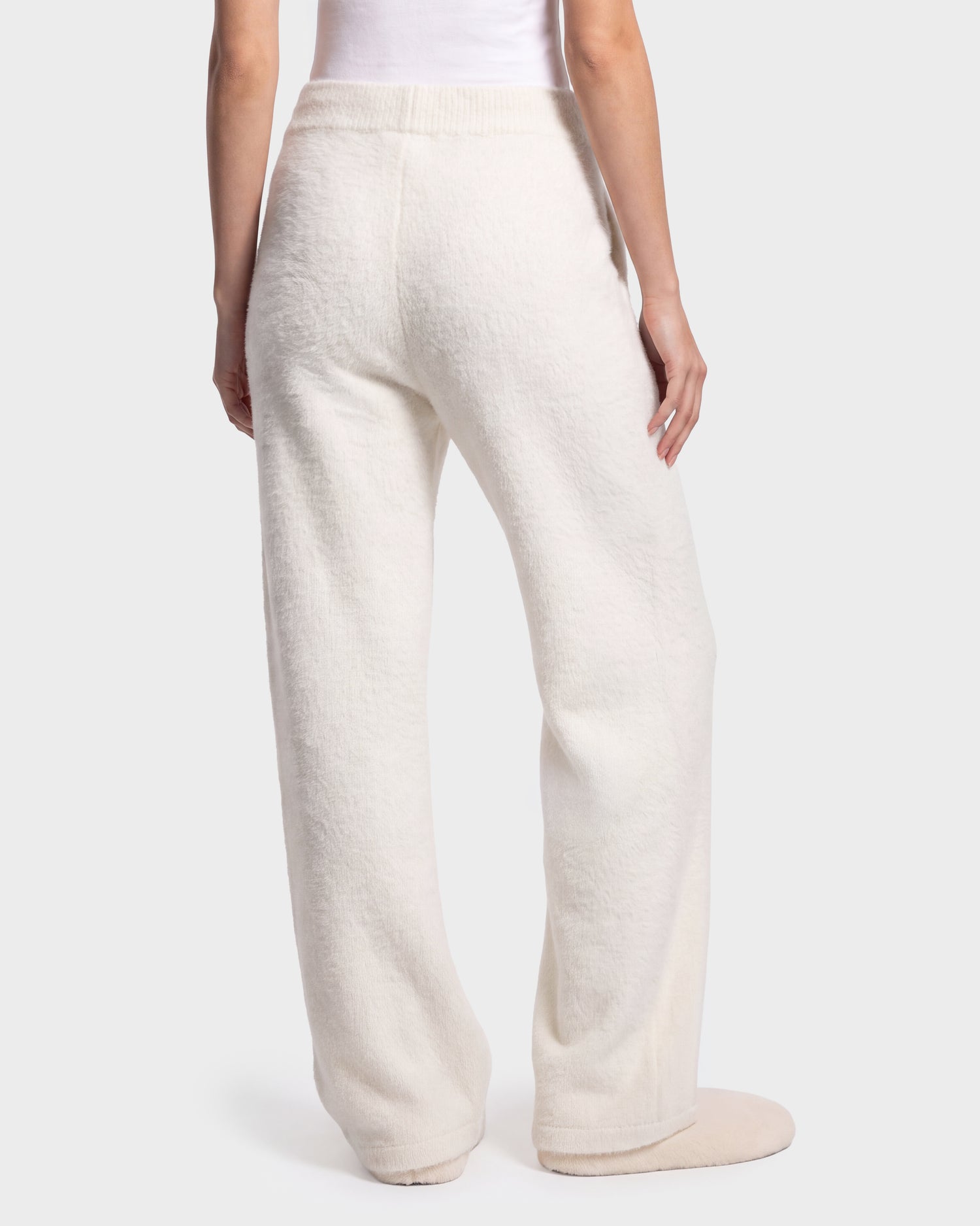 A person shown from the waist down stands against a plain, light-colored background, wearing the Rudsak GENESIS - 8526506 Iceland loose-fitting, textured white pants with matching slippers.