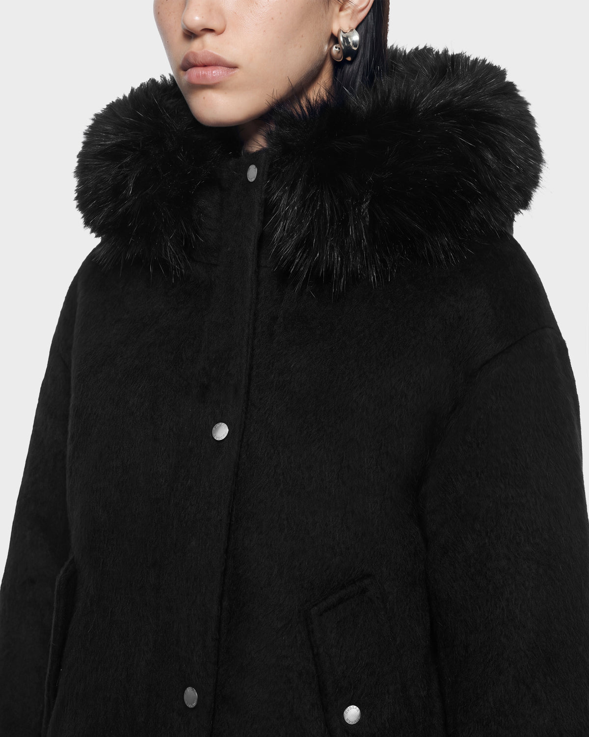 Close-up of a person wearing the HAZEL - 8126981 Black wool-blend winter coat, featuring a black snap-button closure and a thick, detachable faux-fur hood.