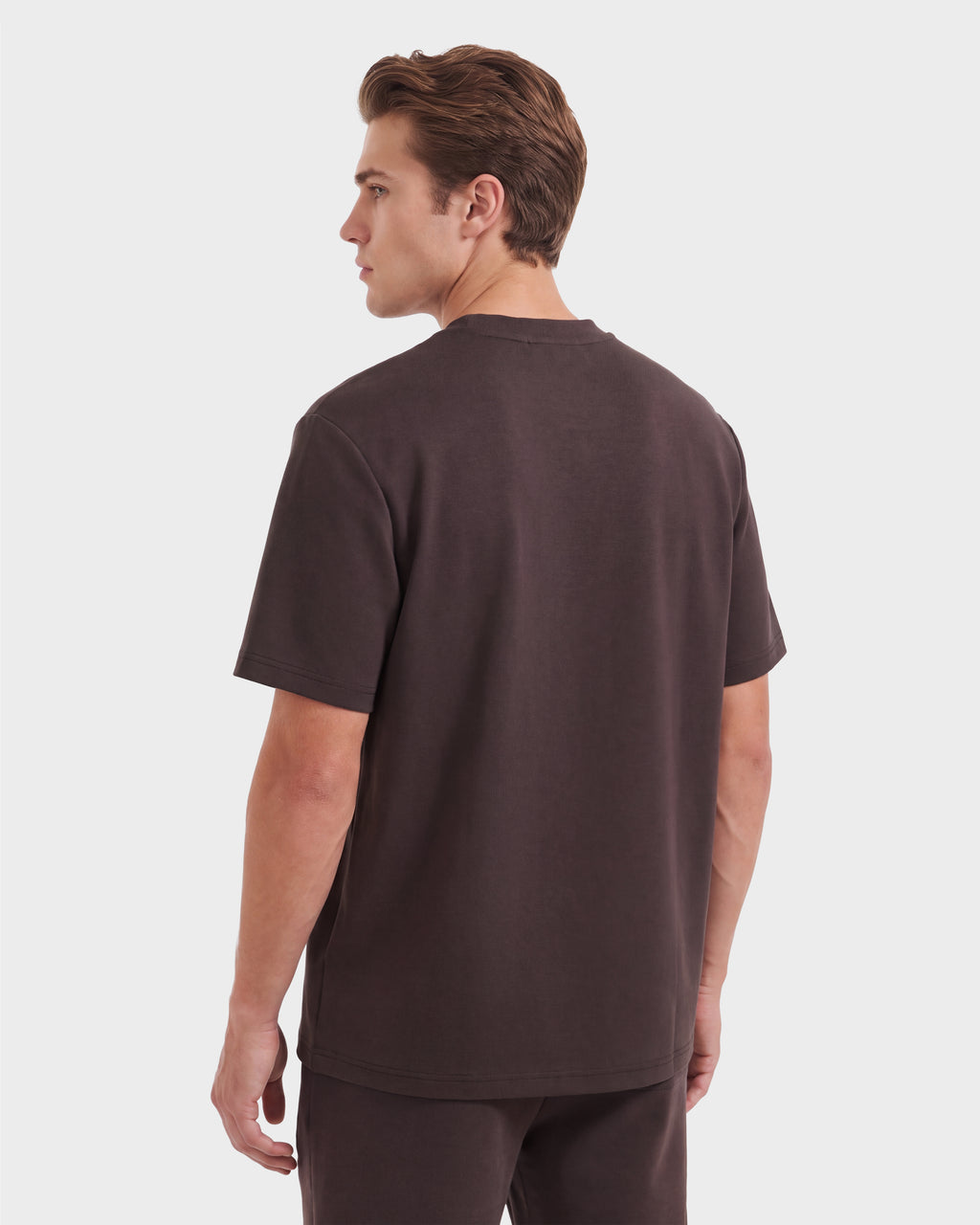 A person stands facing away, wearing the Rudsak KARTER R HV - H525507 Espresso limited edition short-sleeve t-shirt and matching shorts. The background is plain and light-colored.