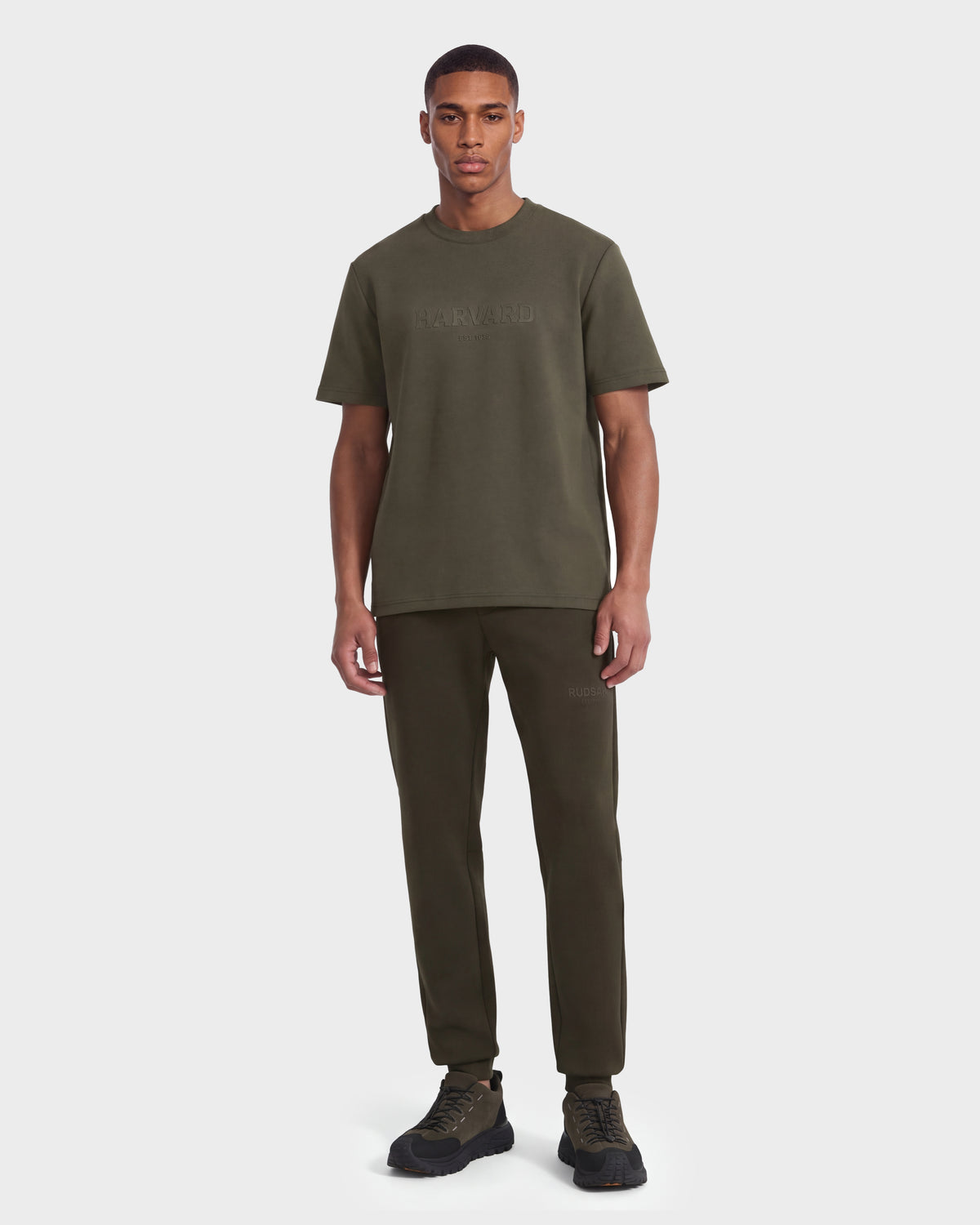 A man stands facing forward against a plain white background, wearing the Rudsak KARTER R HV - H525507 Olive streetwear t-shirt with matching jogger pants and black sneakers.