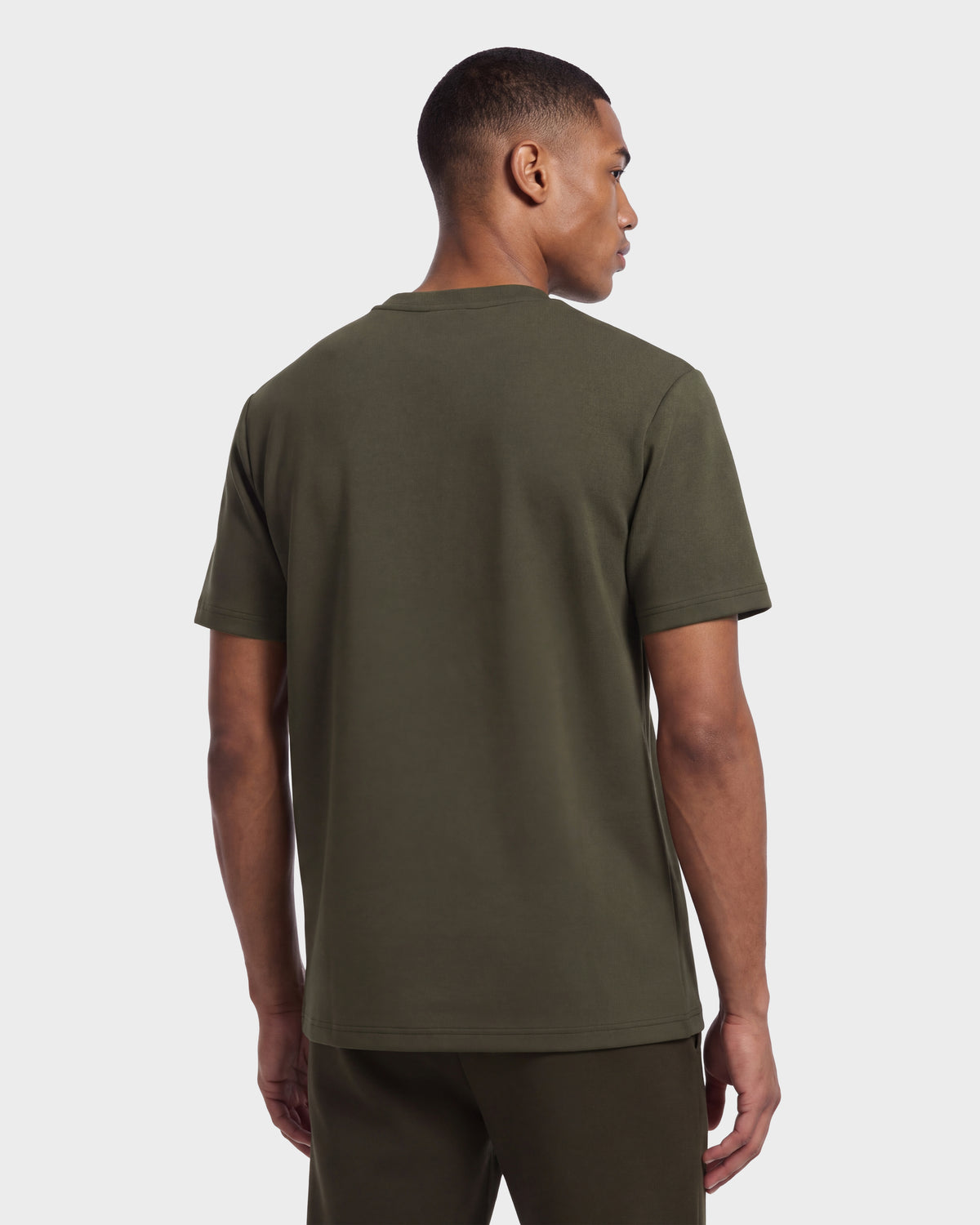 A man stands facing away against a plain light background, wearing the KARTER R HV - H525507 Olive short-sleeve T-shirt and matching pants from Rudsak—an elevated take on streetwear style.