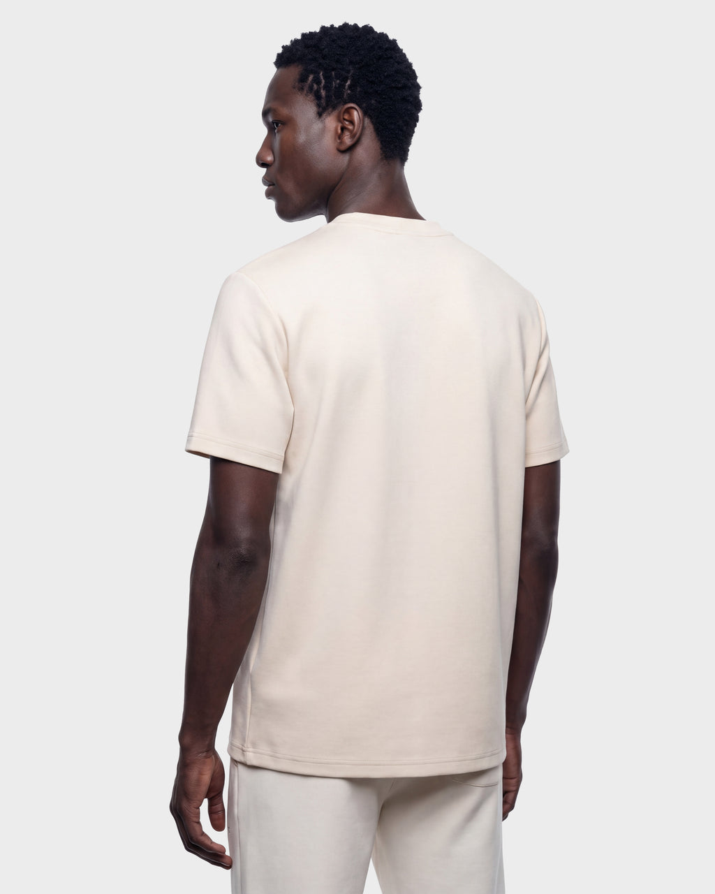 A man wearing the Rudsak KARTER R HV - H525507 Vanilla limited edition cream-colored short-sleeve shirt and matching pants stands facing away, looking to the side against a plain light gray background.
