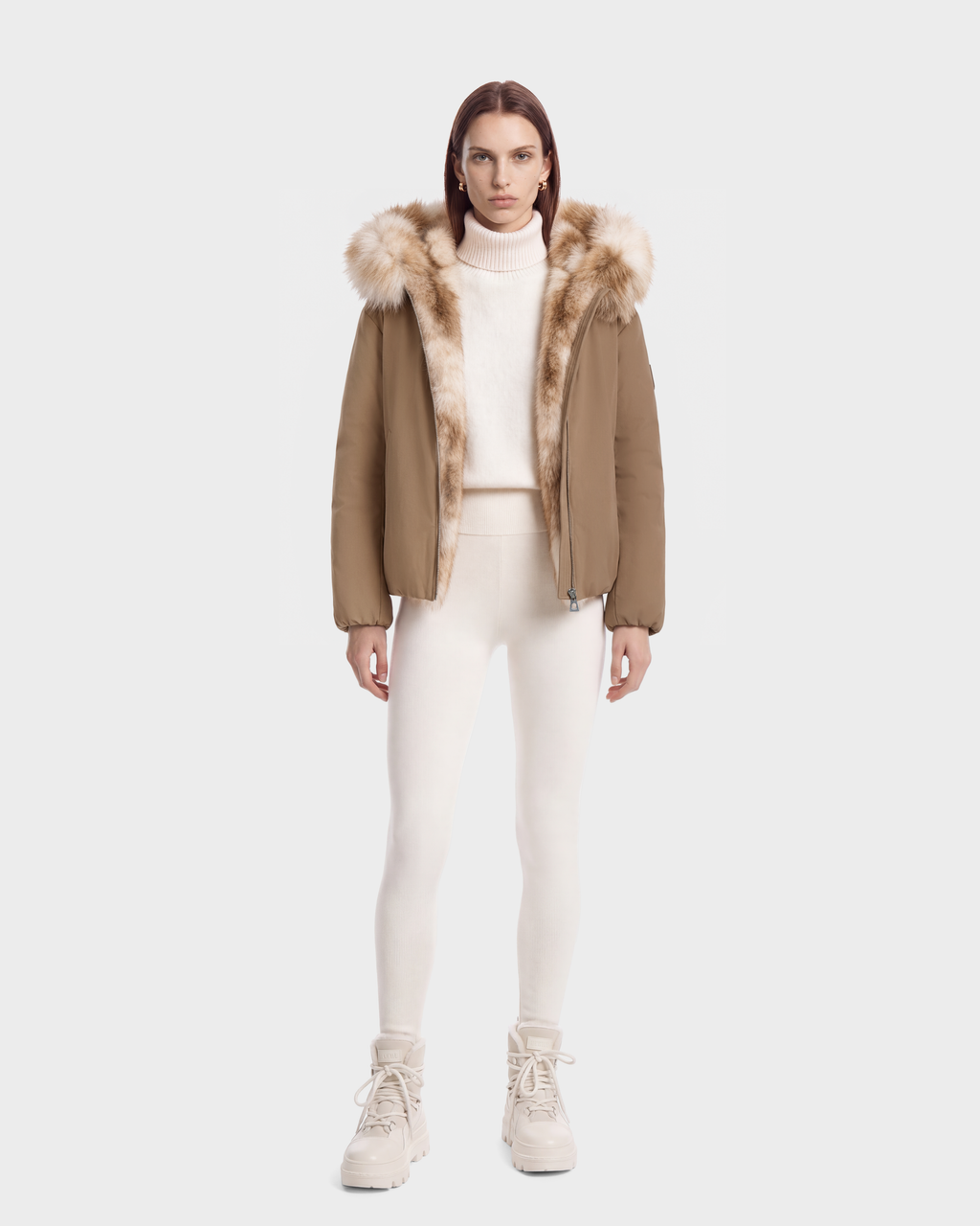 A model wearing a KATHLEEN - 8126764 Sand tan duck down winter bomber jacket with a fur-trimmed collar over a white turtleneck sweater, matching leggings, and platform boots.