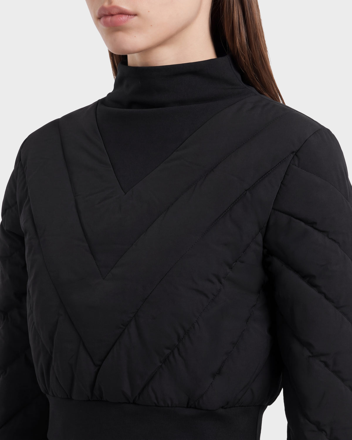 A woman shown from the shoulders up wears the Rudsak KATYA - 8526531 Black jacket, featuring a black quilted, V-patterned design with down insulation and a high-neck black inner layer that evokes après-ski style.