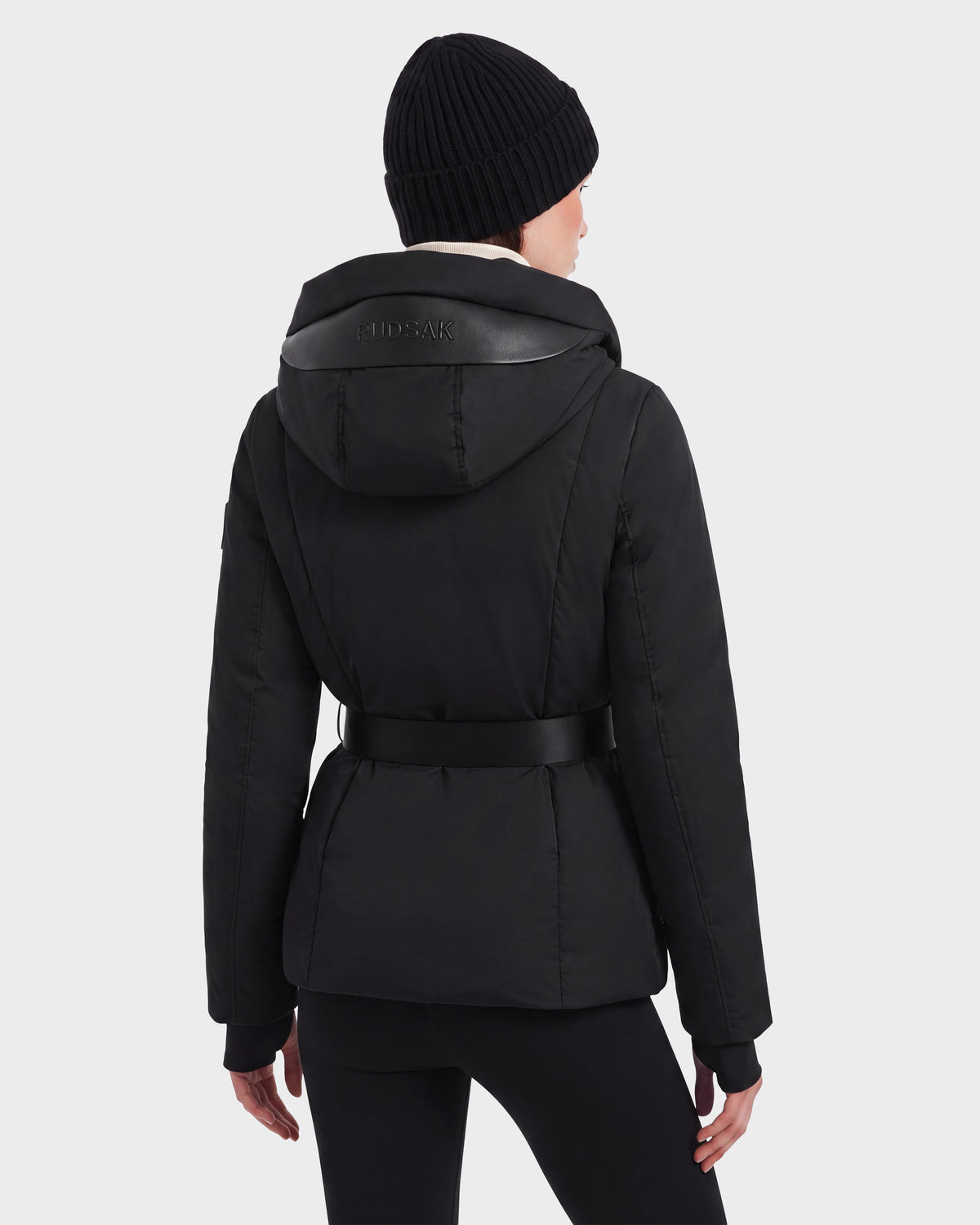 Back view of a person wearing a KOLAD - 8126536 Black short fitted puffer parka with a vegan leather belt and a knit beanie.