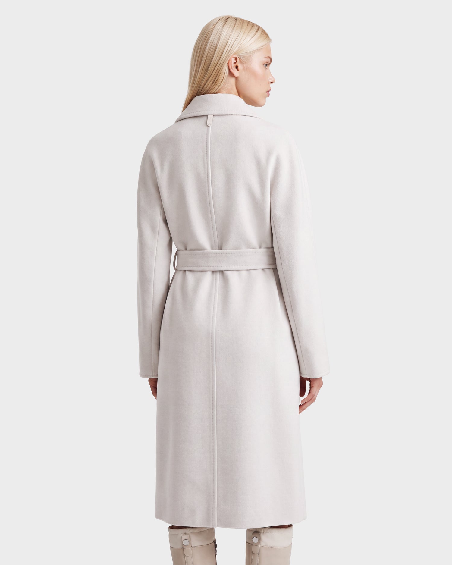 A woman with straight blonde hair stands with her back to the camera against a plain white background, wearing the Rudsak KOURT W - 8124702 Vanilla belted wool coat over light pants.