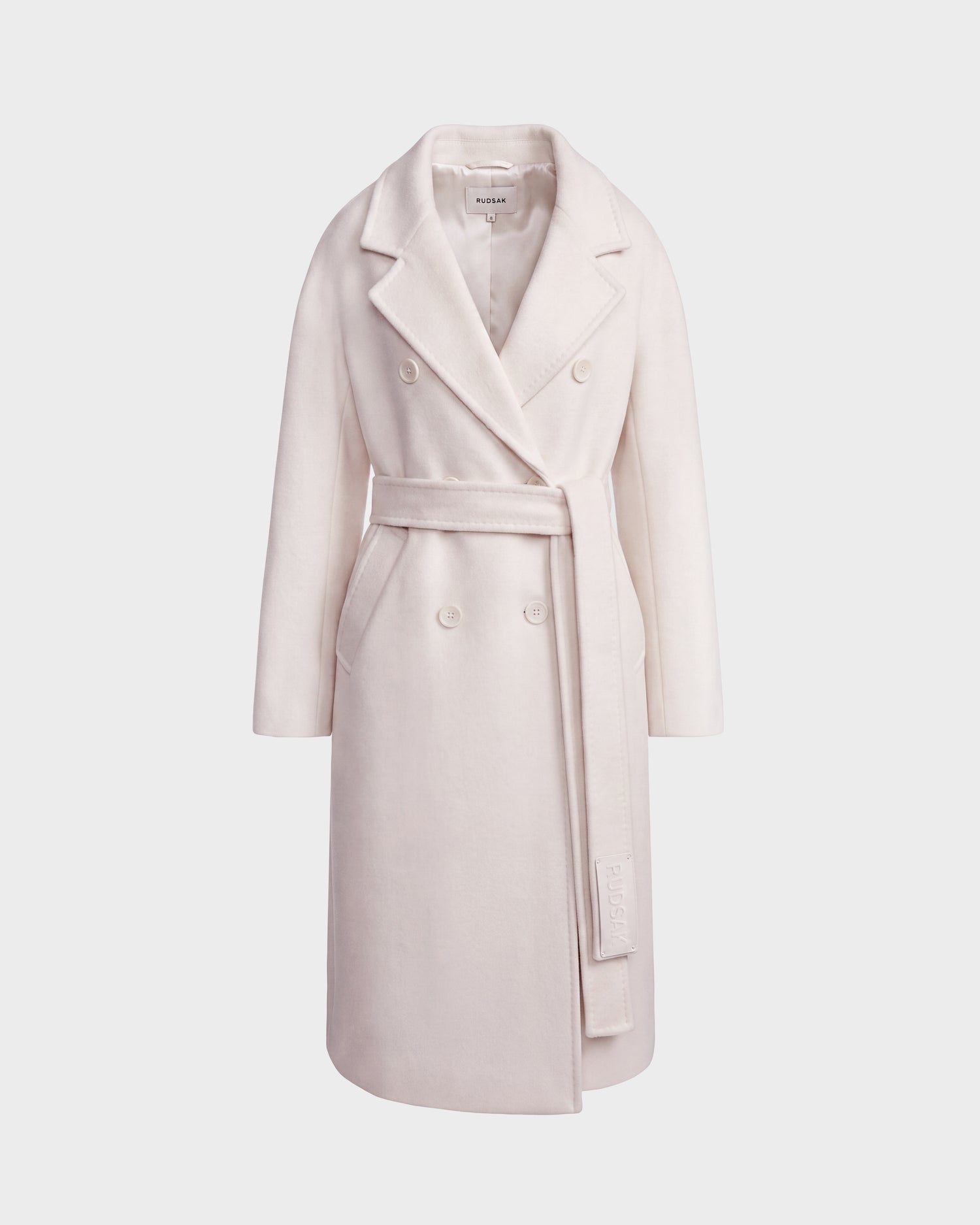 The Rudsak KOURT W - 8124702 Vanilla is a long, light beige women’s wool coat featuring a wide lapel collar and a matching belt tied at the waist, shown against a plain white background.