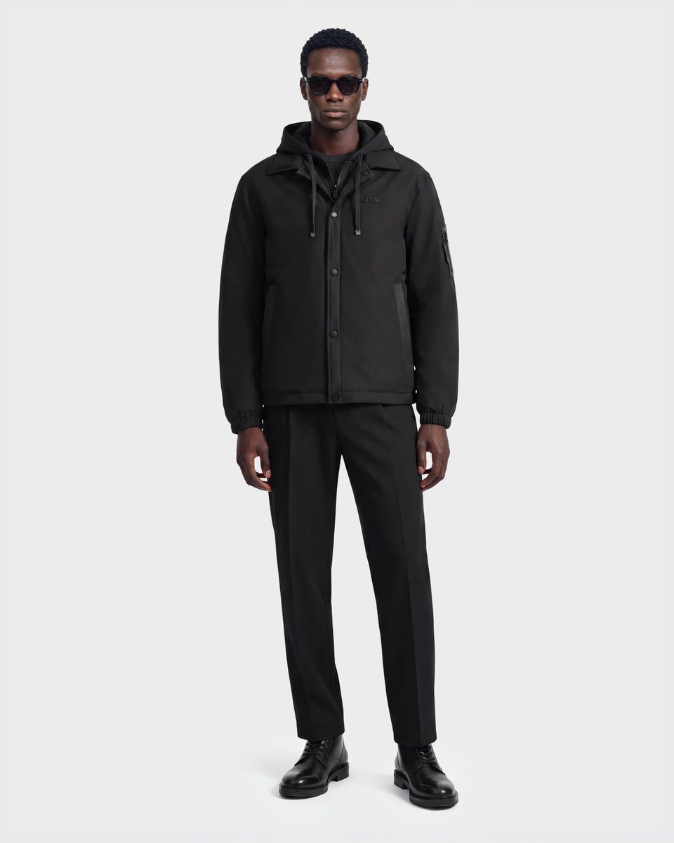 A man wearing sunglasses and the Rudsak LUCA - 6125009 Black weather-resistant hooded men’s jacket, along with black pants and black shoes, stands facing forward against a plain white background.