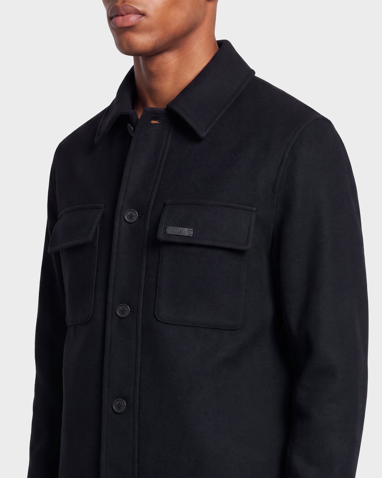 A person wearing the Rudsak MACKENZIE - 6126715 Black men’s wool-blend shirt jacket, featuring two front chest pockets, shown from shoulders to waist against a plain light background—perfect for transitional layering.