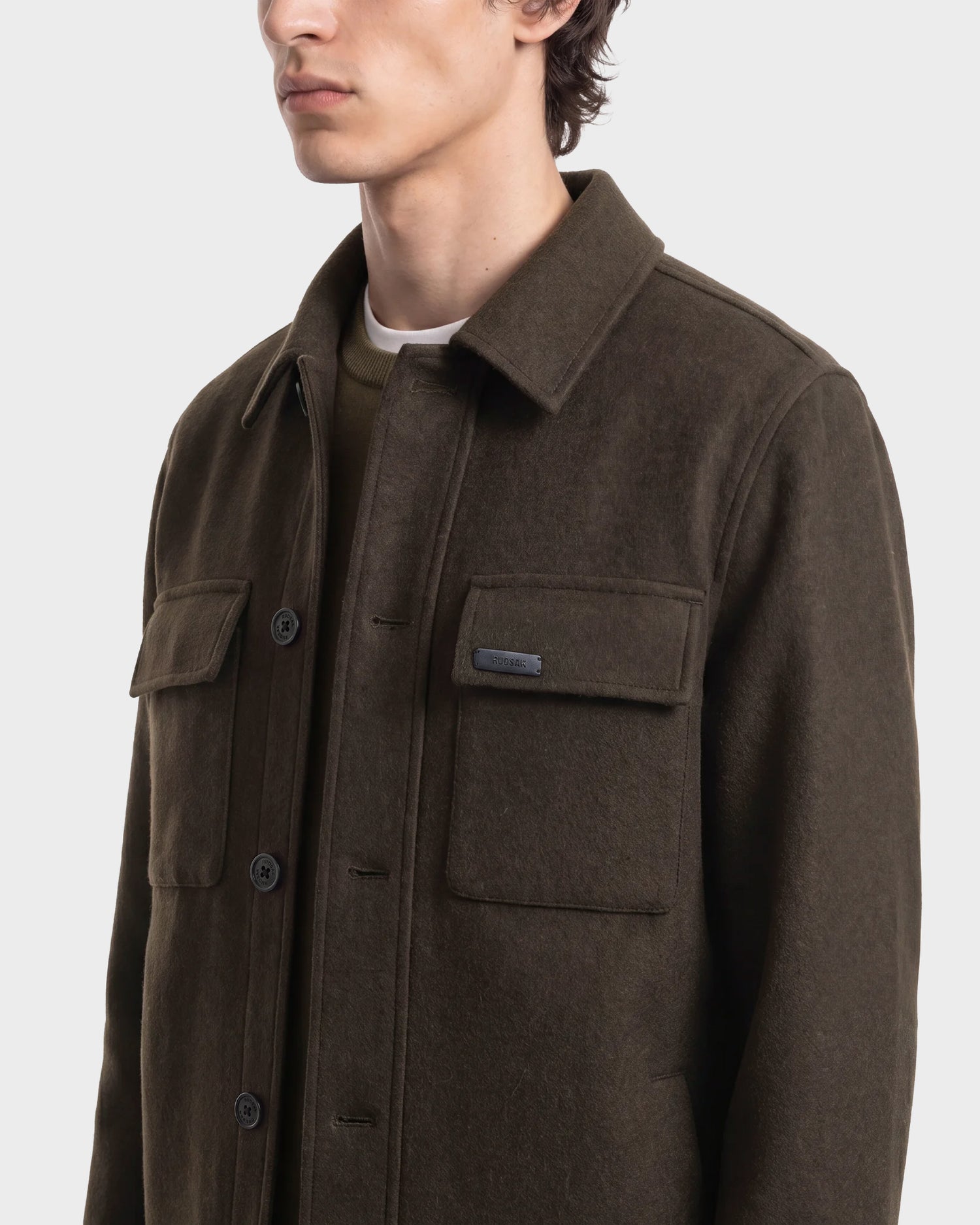A person wearing the Rudsak MACKENZIE - 6126715 Olive wool blend men’s shirt jacket with two front flap pockets, shown from the chest up against a plain light background.