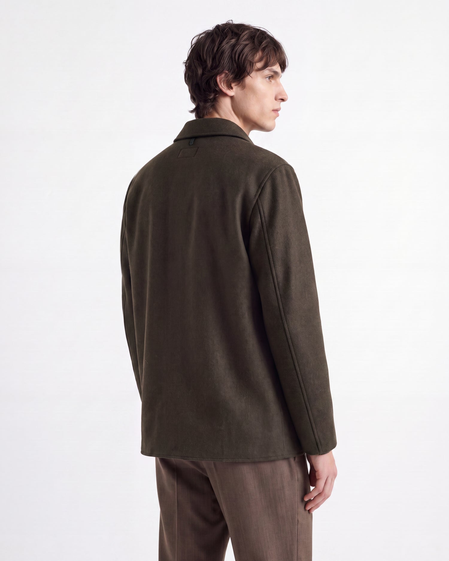 A person with short, wavy brown hair is seen from behind, wearing the Rudsak MACKENZIE - 6126715 Olive men’s shirt jacket in a soft wool blend and brown pants against a plain white background.