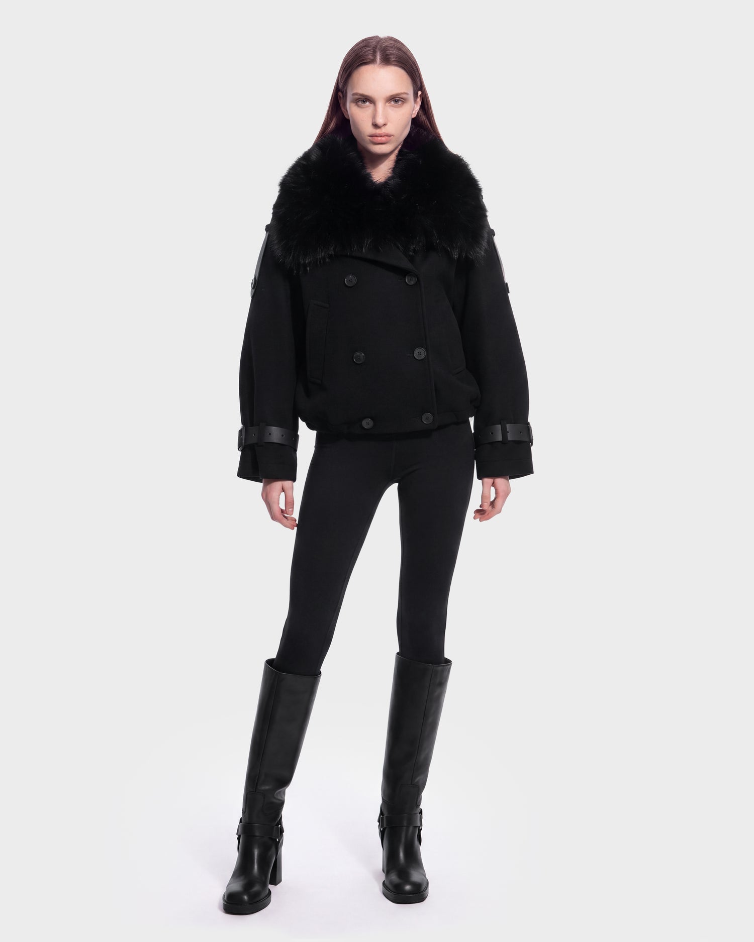 A person stands facing forward, wearing the MAEMI - 8126985 Black jacket by Rudsak, paired with black leggings and knee-high black boots, against a plain white background. This stylish look is available for pre-order and is expected to ship by September 15th.
