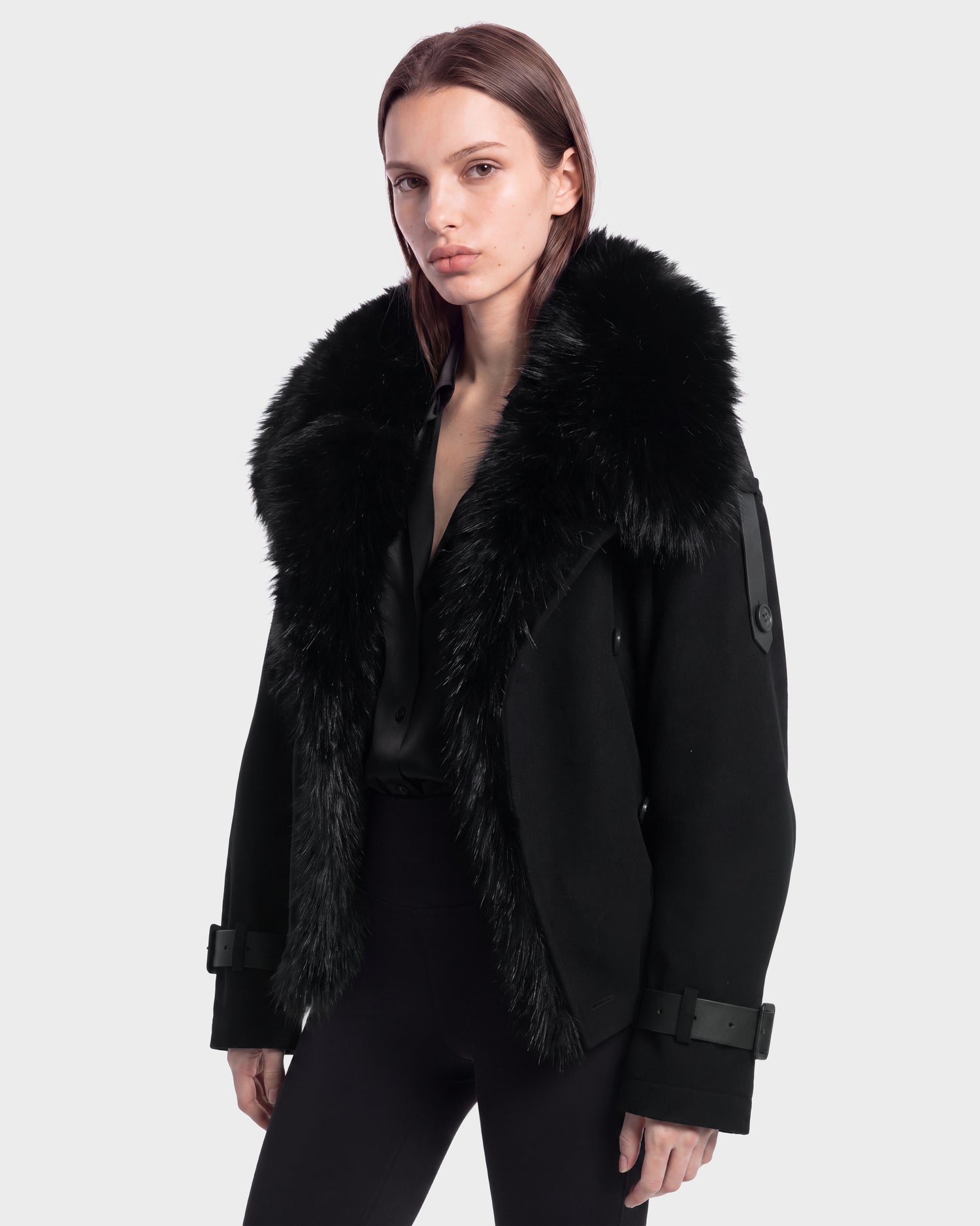A model is wearing the Rudsak MAEMI - 8126985 Black jacket, featuring a large, fluffy faux fur collar, styled with a black shirt and black pants against a plain light gray background. This look is available for pre-order and is expected to ship by September 15th.