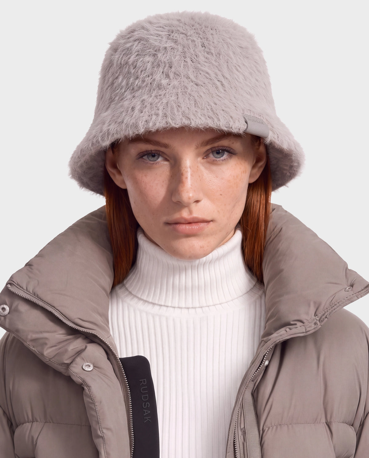 A person wearing a grey fuzzy MAIE - 8426517 Cement bucket hat and a puffer jacket over a white turtleneck.