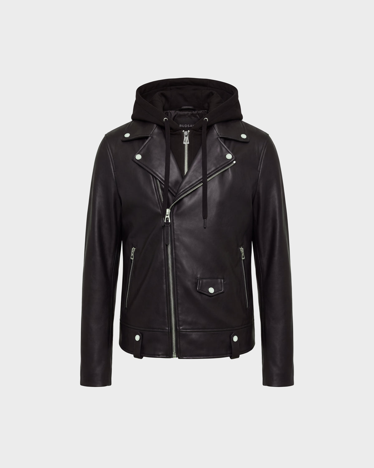 The MANUS - 6124600 Black men’s leather moto jacket by Rudsak features black leather construction with silver zippers and buttons, an asymmetrical front zip, two zippered pockets, a flap pocket on the front, and a removable hooded dickie for added versatility. The background is light gray.