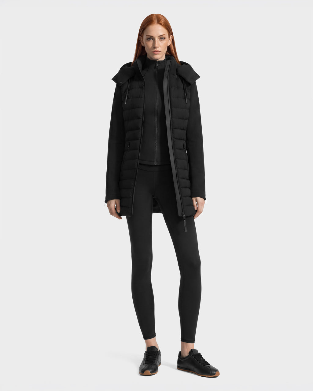 A woman wearing a black Rudsak MERINA - 8125056 quilted down jacket under a matching hooded vest, paired with leggings and black sneakers.