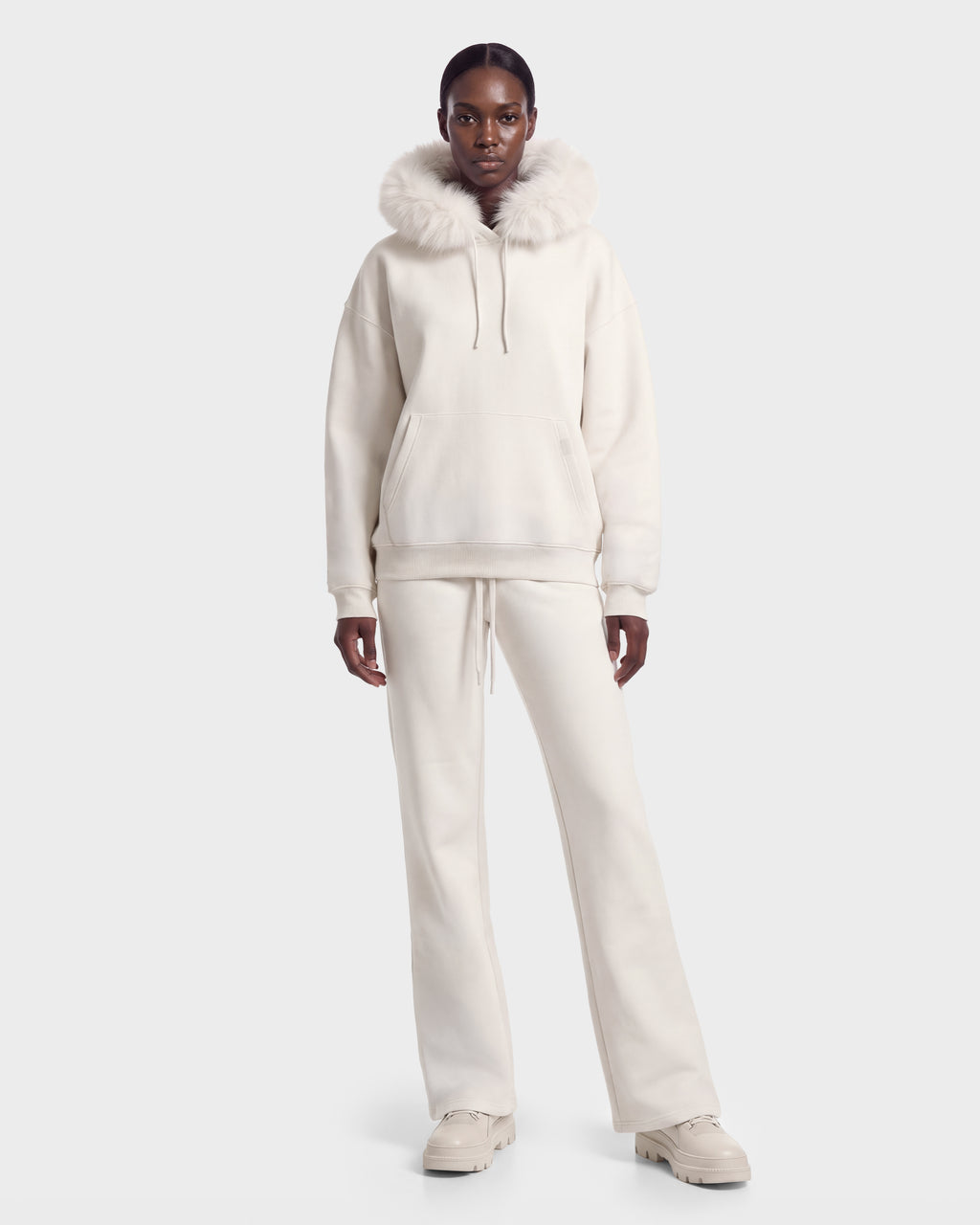 A person faces forward in the Rudsak MILENA - 8526689 Vanilla plush hoodie and matching pants with faux-fur trim, paired with beige chunky shoes, against a plain light background.
