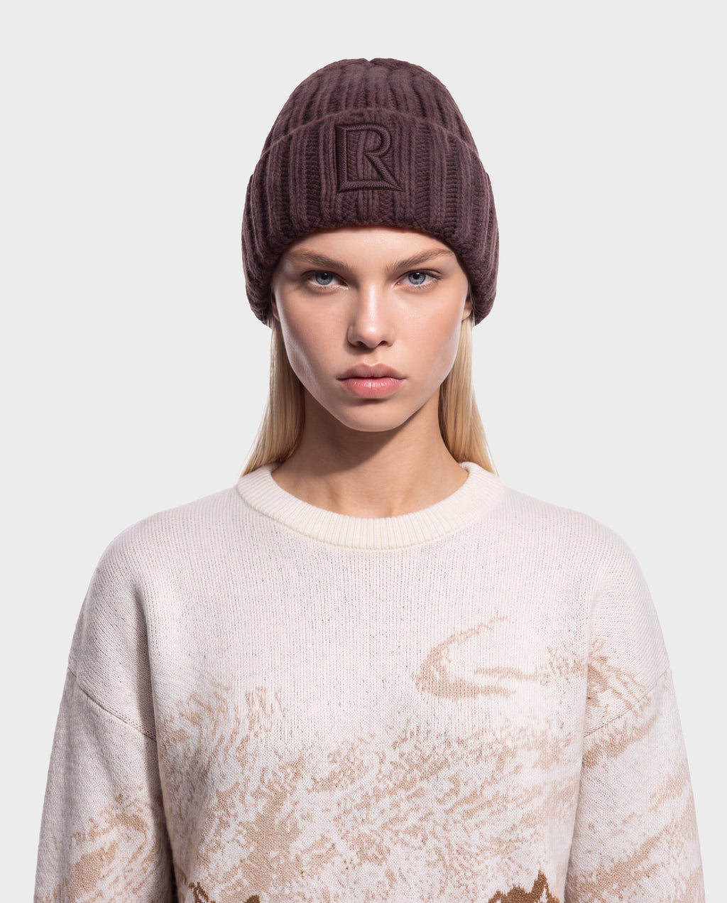 A person wearing a dark brown MISSA - 8426512 Espresso ribbed knit beanie with a square logo patch featuring a letter R on the front.