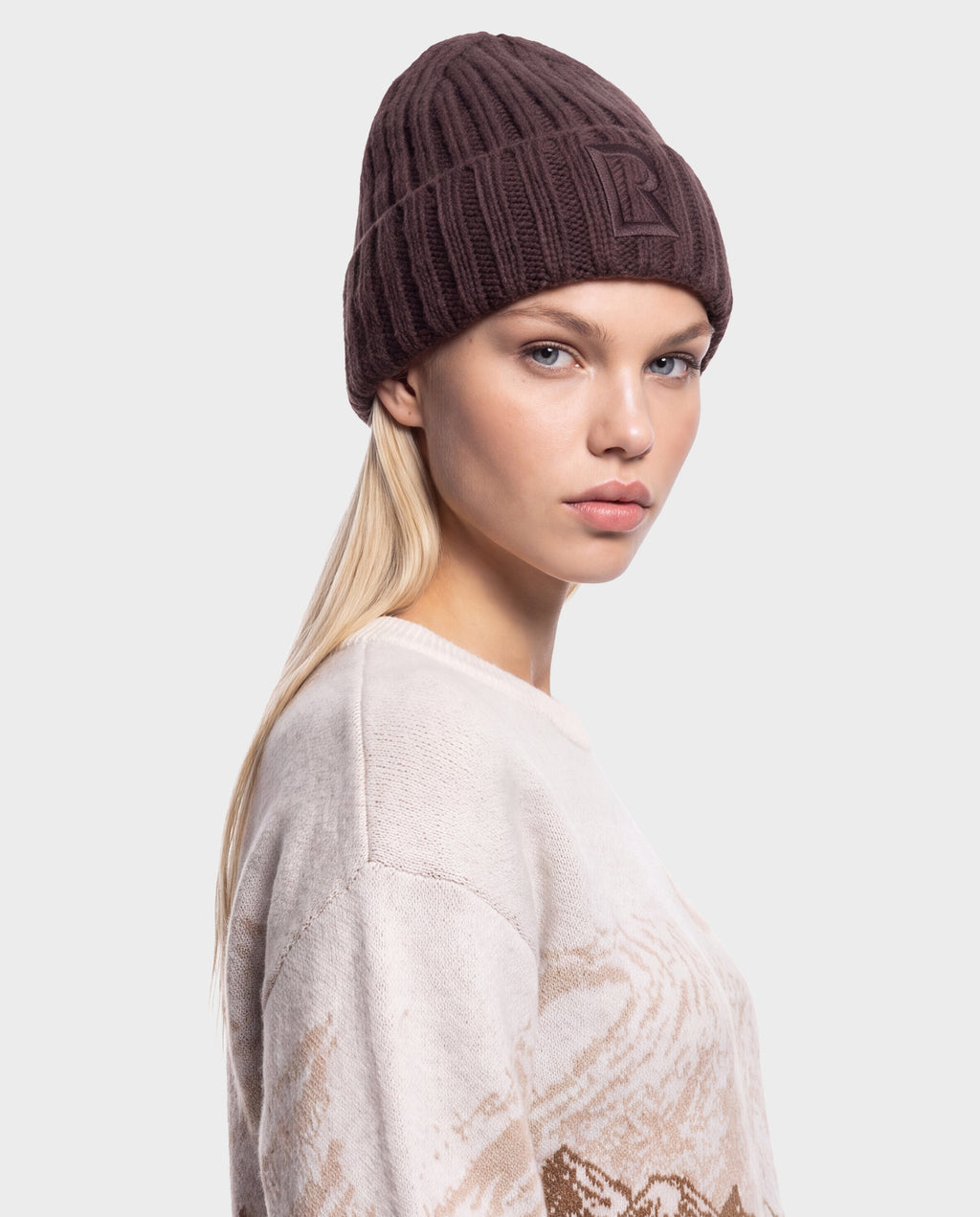 A person wearing a MISSA - 8426512 Espresso dark brown ribbed knit beanie with an embossed logo on the cuff.