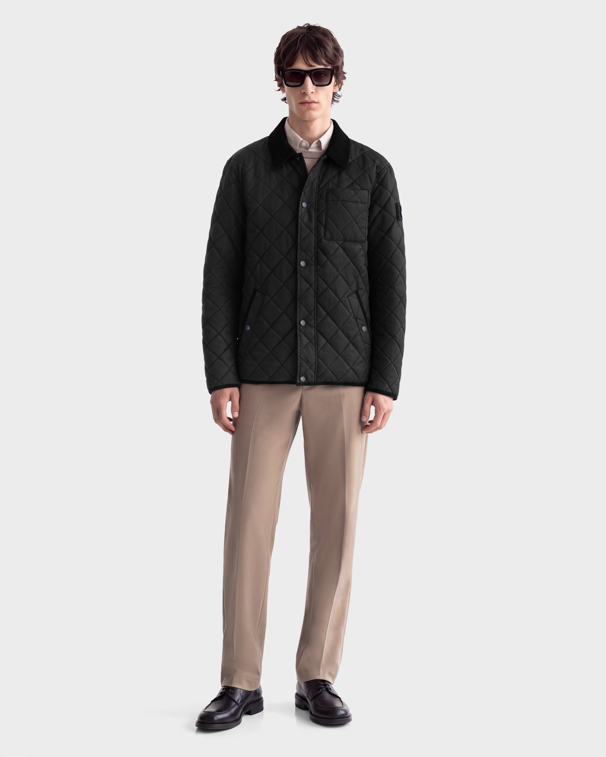 A person wearing a black Rudsak MONTY - 6126722 Black quilted jacket for lightweight insulation over a collared shirt, paired with tan trousers and black loafers.