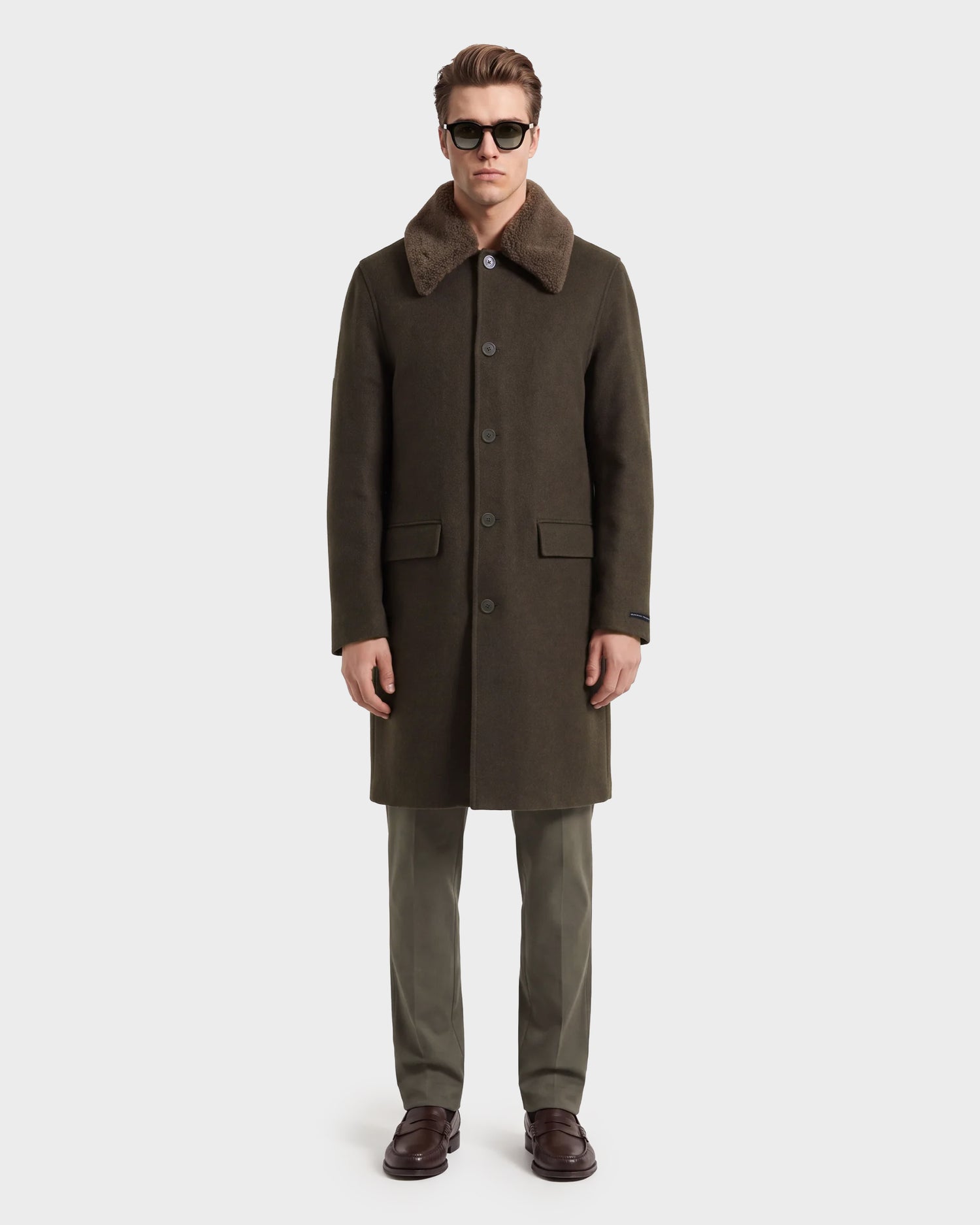 A man wearing sunglasses, a dark green wool blend overcoat with a brown fur collar, Rudsak’s NICO - 6126717 Olive trousers, and brown dress shoes stands facing forward against a plain white background—an ideal look for transitional layering.