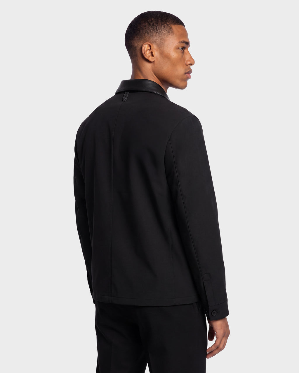 A man stands facing sideways, wearing the Rudsak PALMER - 6125002 Black shirt jacket and matching pants against a plain white background.