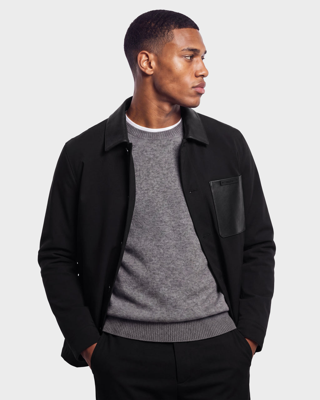 A man wearing the Rudsak PALMER - 6125002 Black eco-fill jacket over a gray sweater stands with his hands in his pockets, looking to his right against a plain light background—showcasing a true men’s wardrobe essential.