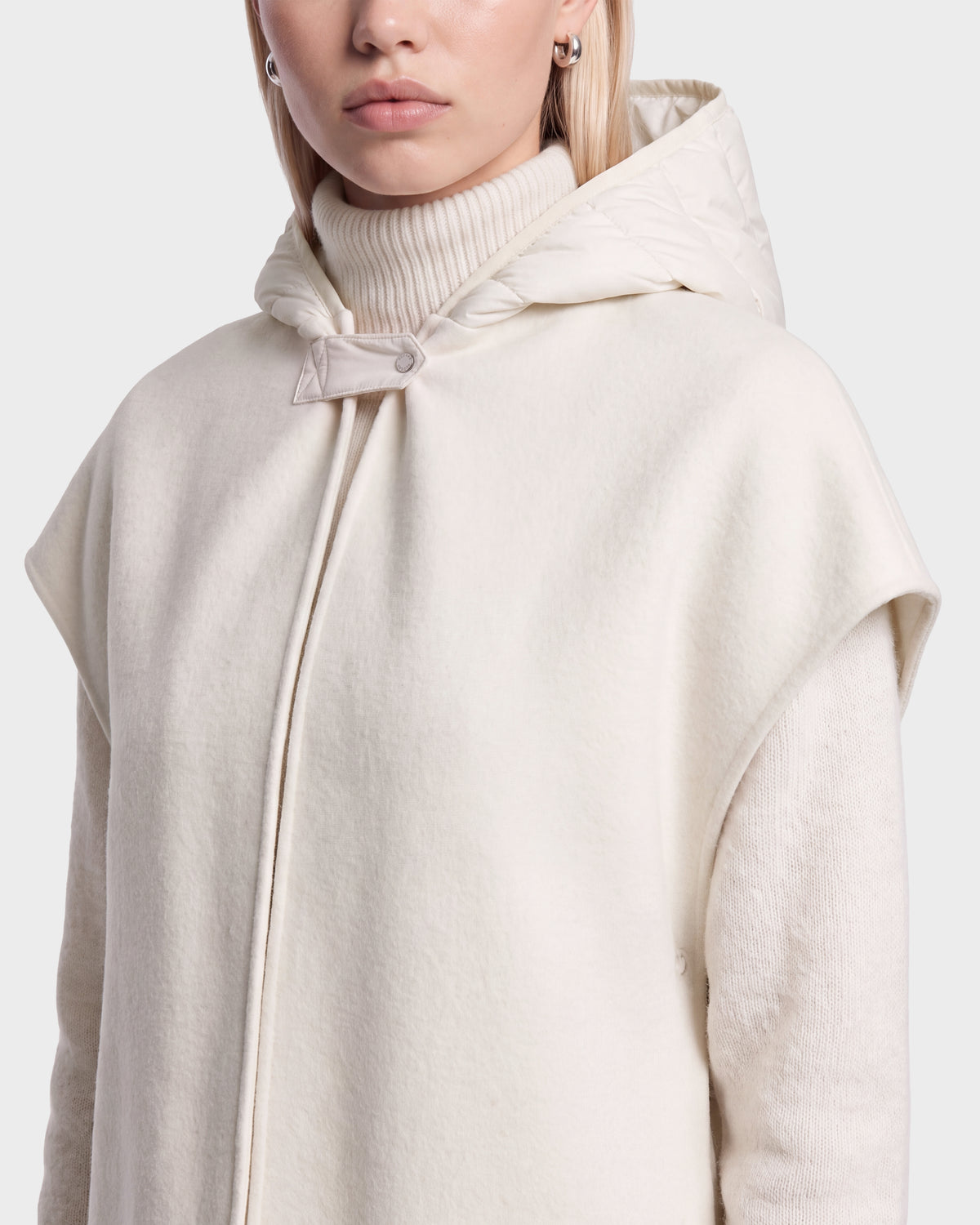 A person wearing the ROXANE - 8526677 Vanilla hooded cape by Rudsak over a cream turtleneck sweater, featuring short sleeves and a single button at the neck. Only the lower half of their face is visible.
