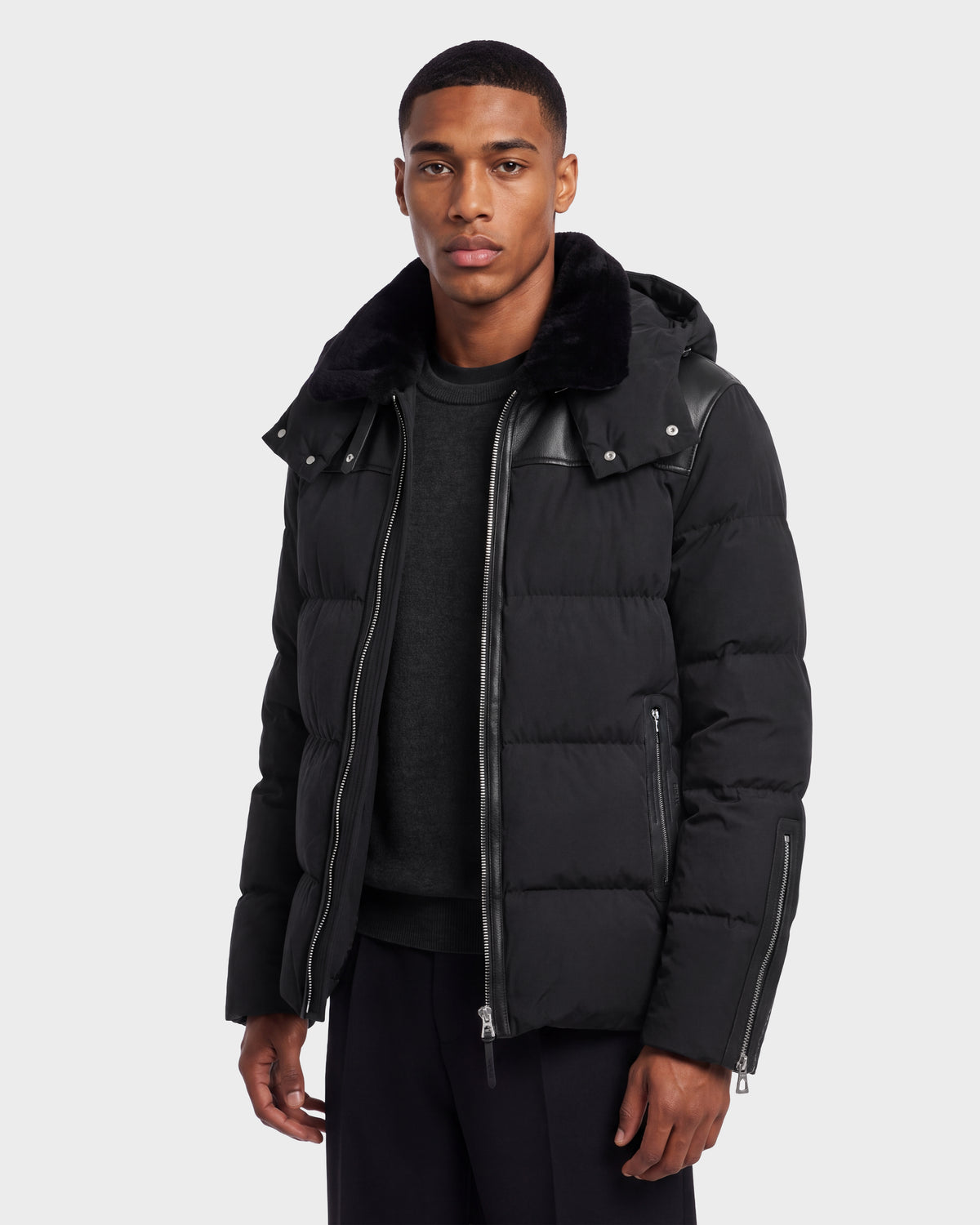 A man wearing a black Rudsak SIMON PX - 6126503 Black quilted puffer jacket with leather trim and a faux-fur collar.