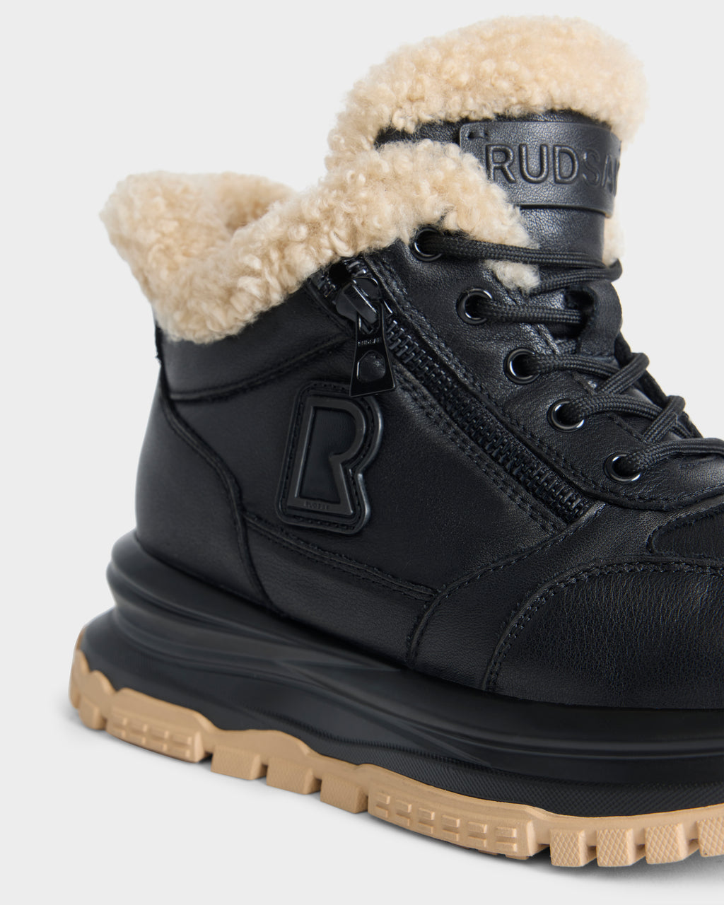 Rudsak VIONA - L226508 Black ankle boot with a beige shearling lining, a side zipper, and a thick, lugged beige sole.