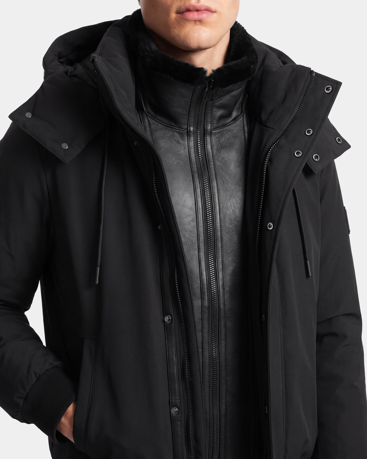 A person wearing the Rudsak WILL - 6126561 Black hooded jacket layered over a black leather zip-up jacket, shown from the shoulders to the mouth against a plain background.