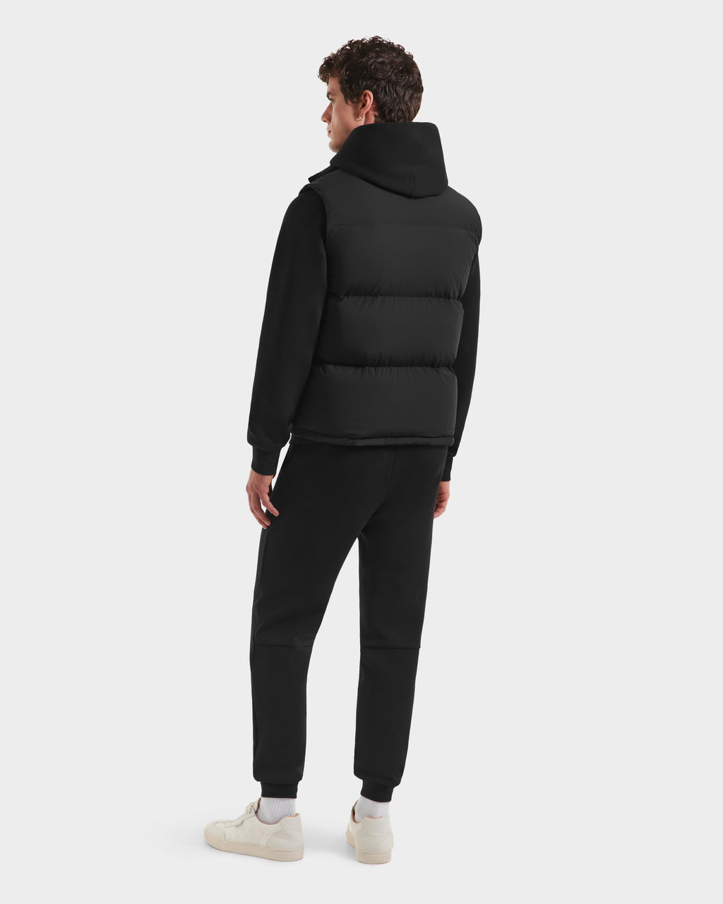 A person wearing the Rudsak FREDDY HV - H125510 Black hoodie, black pants, and white sneakers stands facing away, looking to the left against a plain white background.
