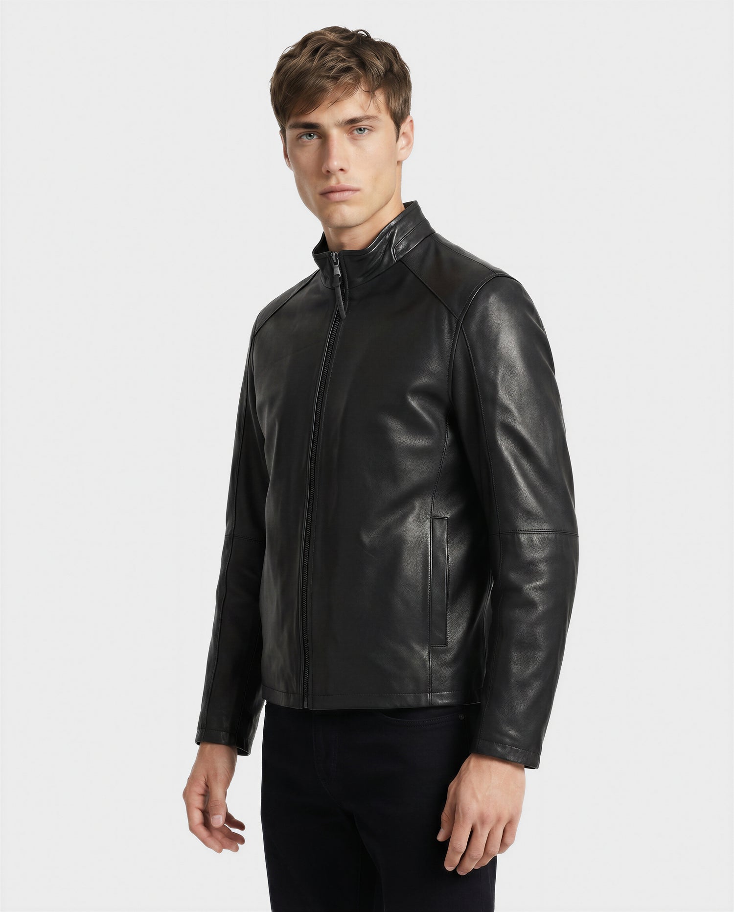 A young man with short brown hair and a neutral expression stands against a plain white background, wearing the Rudsak GARY - M126061 Black fitted leather jacket featuring a zip-up front and high collar.
