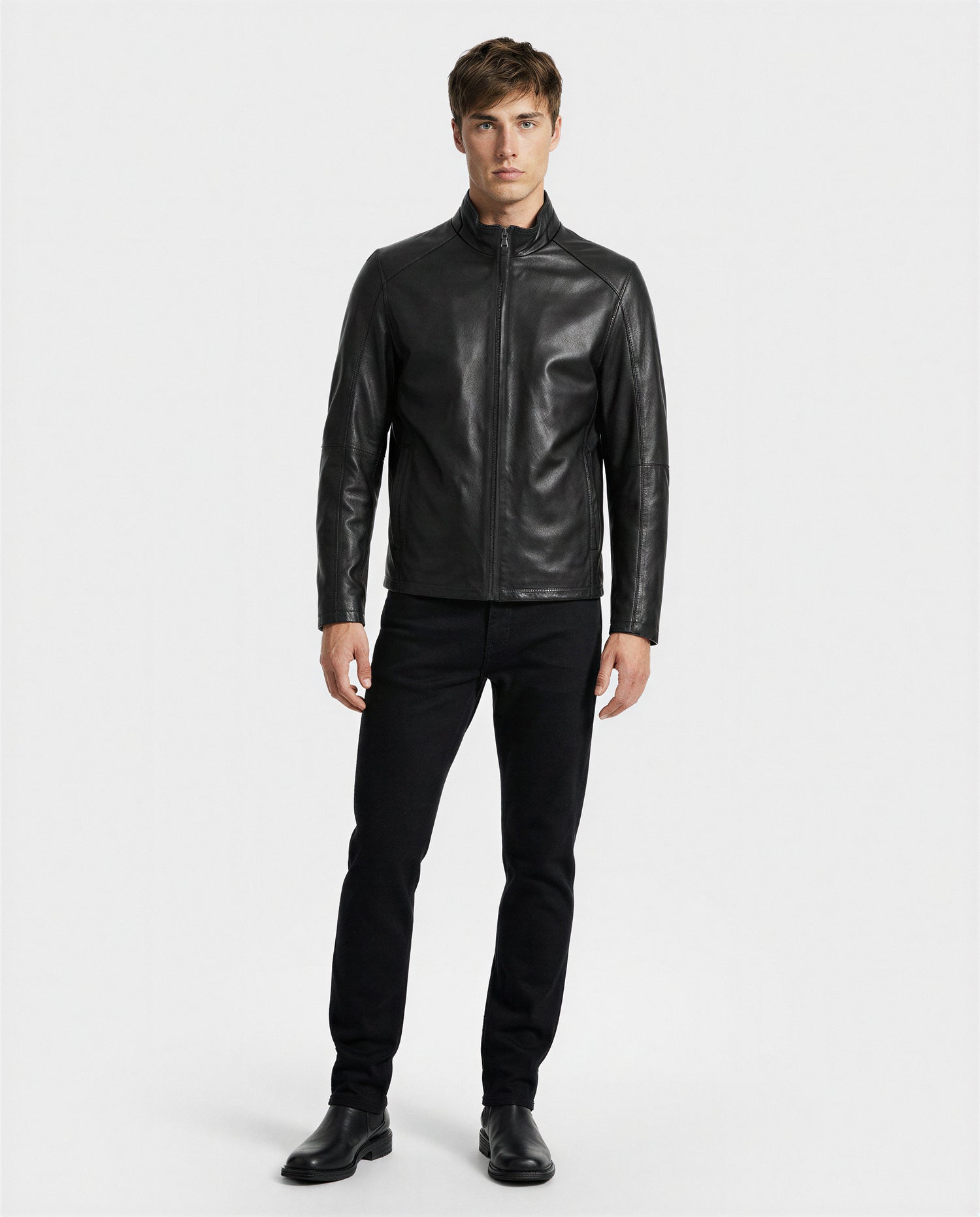 A man stands against a plain white background wearing the Rudsak GARY - M126061 Black jacket, black jeans, and black shoes. He faces forward with a neutral expression and his arms by his sides.
