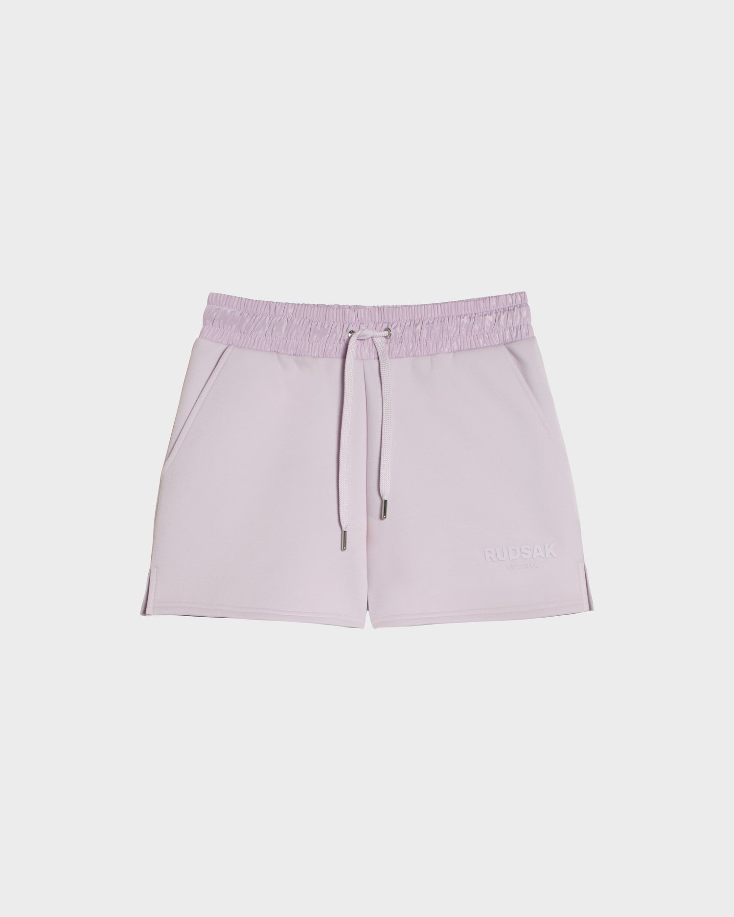 The GENEVA - 8524070 Lilac Foam womens shorts by Rudsak feature a sporty look with an elastic waistband, two side pockets, subtle stitching, and RUDSAK branding on the lower left leg, shown on a white background.