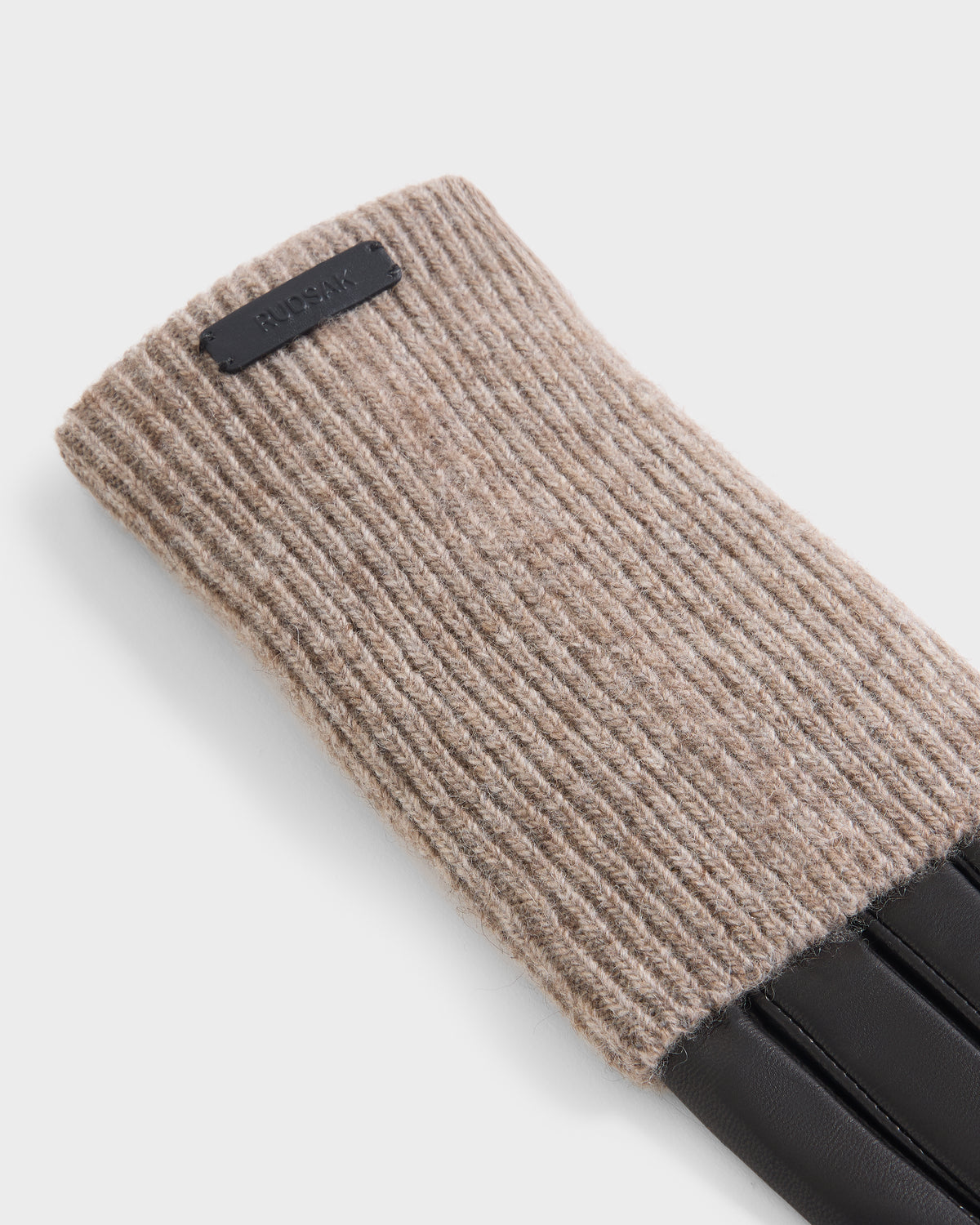 A close-up of chic fall accessories: Rudsak’s MARINE - 8424516 glove in Black/Camel, featuring a ribbed beige knit cuff and sleek black leather fingers, set against a plain light background. This elegant piece perfectly captures the timeless appeal of women’s leather gloves with the cozy texture of knit wool gloves.