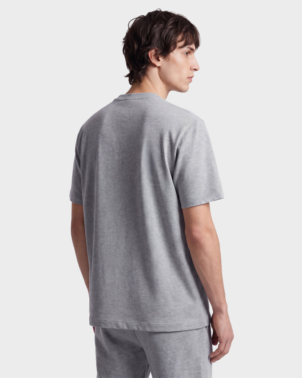 A young man with short brown hair is wearing the Rudsak GRANT - 6525036 Heather Grey crewneck men’s tee and matching shorts, standing and facing away while looking over his left shoulder against a plain white background. The t-shirt is crafted from premium cotton for added comfort and style.